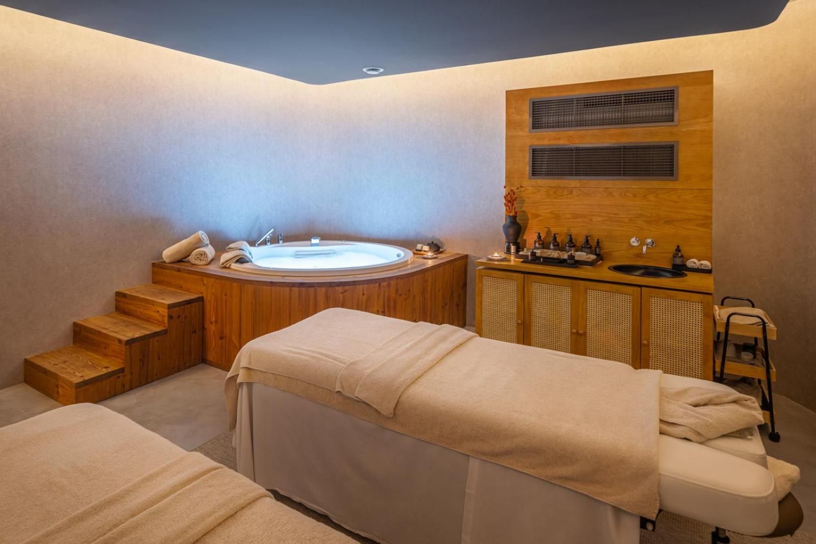 Warm teak surrounds and gentle lighting transform the spa treatment room into a sanctuary, where couples massage tables await beside a sunken soaking tub.