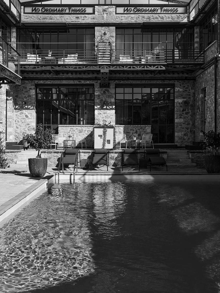 Stone walls frame a serene courtyard pool where industrial-chic balconies cast geometric shadows across dark water, creating an intimate urban oasis.
