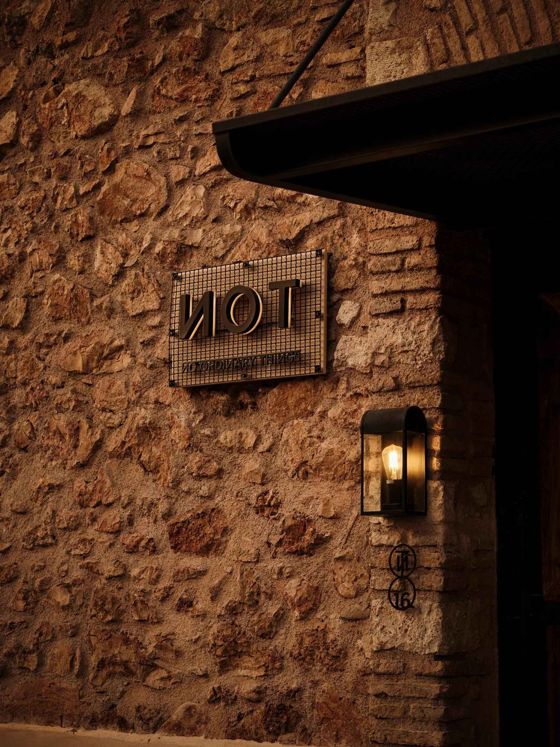 Warm lantern light illuminates rough-hewn stone walls and the hotel's distinctive signage, creating an intimate Mediterranean atmosphere as evening settles over this boutique retreat.