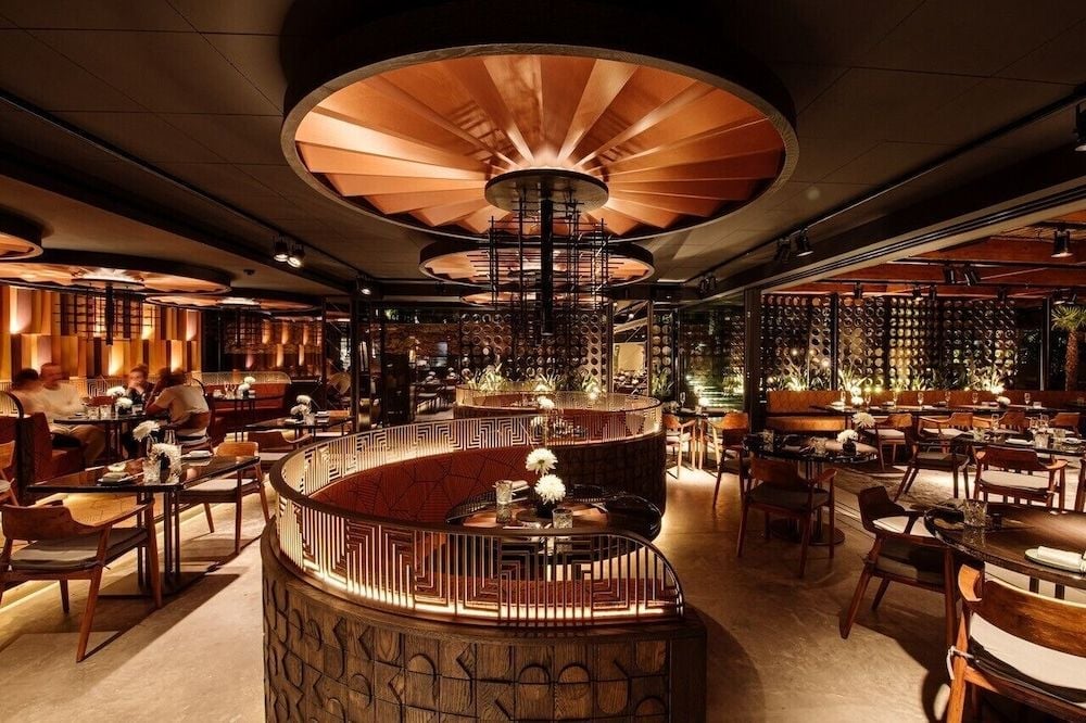 Warm copper ceiling medallions cast golden light over timber tables and woven screens, creating an intimate dining cocoon where modern elegance meets artisanal craftsmanship.