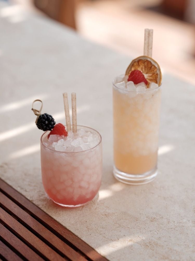 Artfully crafted cocktails catch golden hour light on sun-dappled stone, where blackberry-garnished libations and dried citrus wheels elevate the poolside drinking ritual.