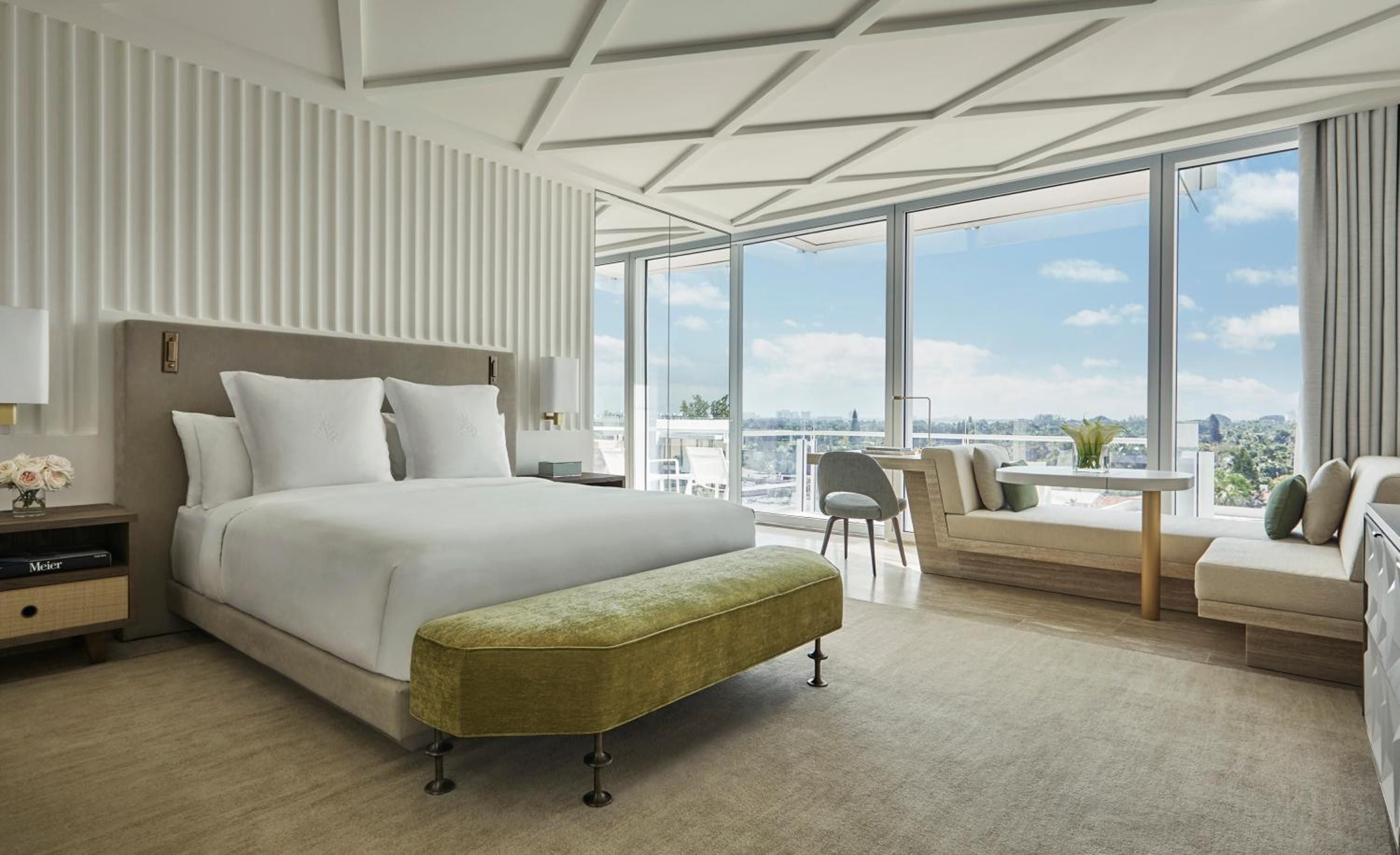 Floor-to-ceiling windows frame Miami's skyline from this serene suite, where white linens and sage accents create a sophisticated retreat above the Atlantic coastline.