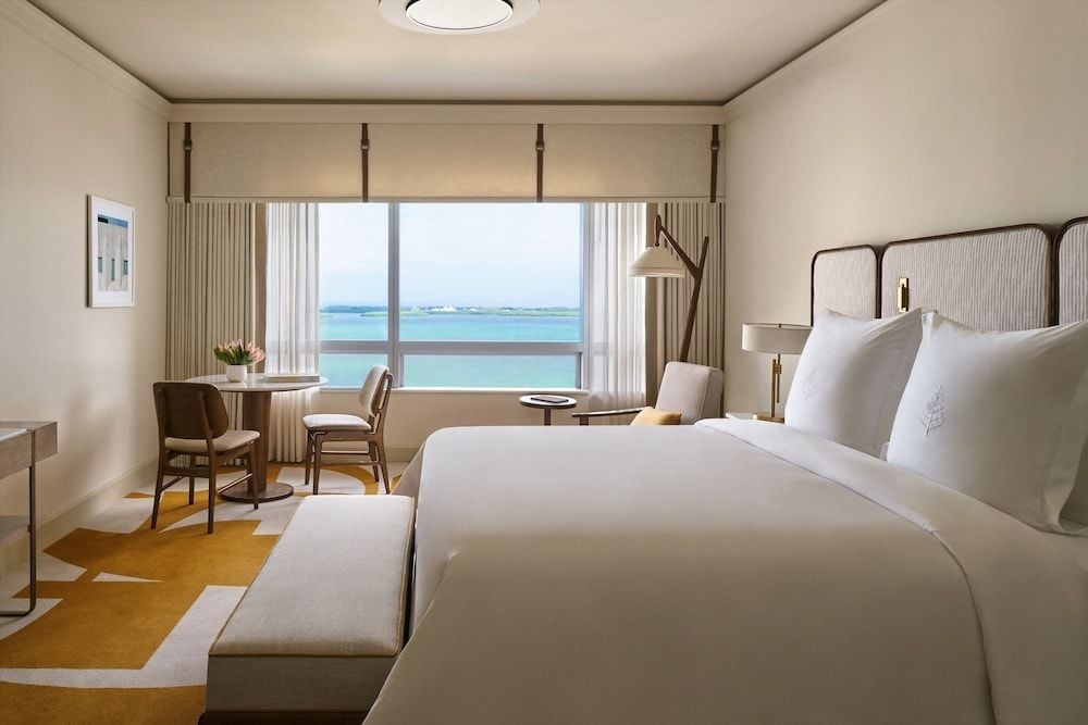 Crisp white linens and warm neutral tones frame floor-to-ceiling windows overlooking Biscayne Bay, where turquoise waters stretch toward the Miami skyline.