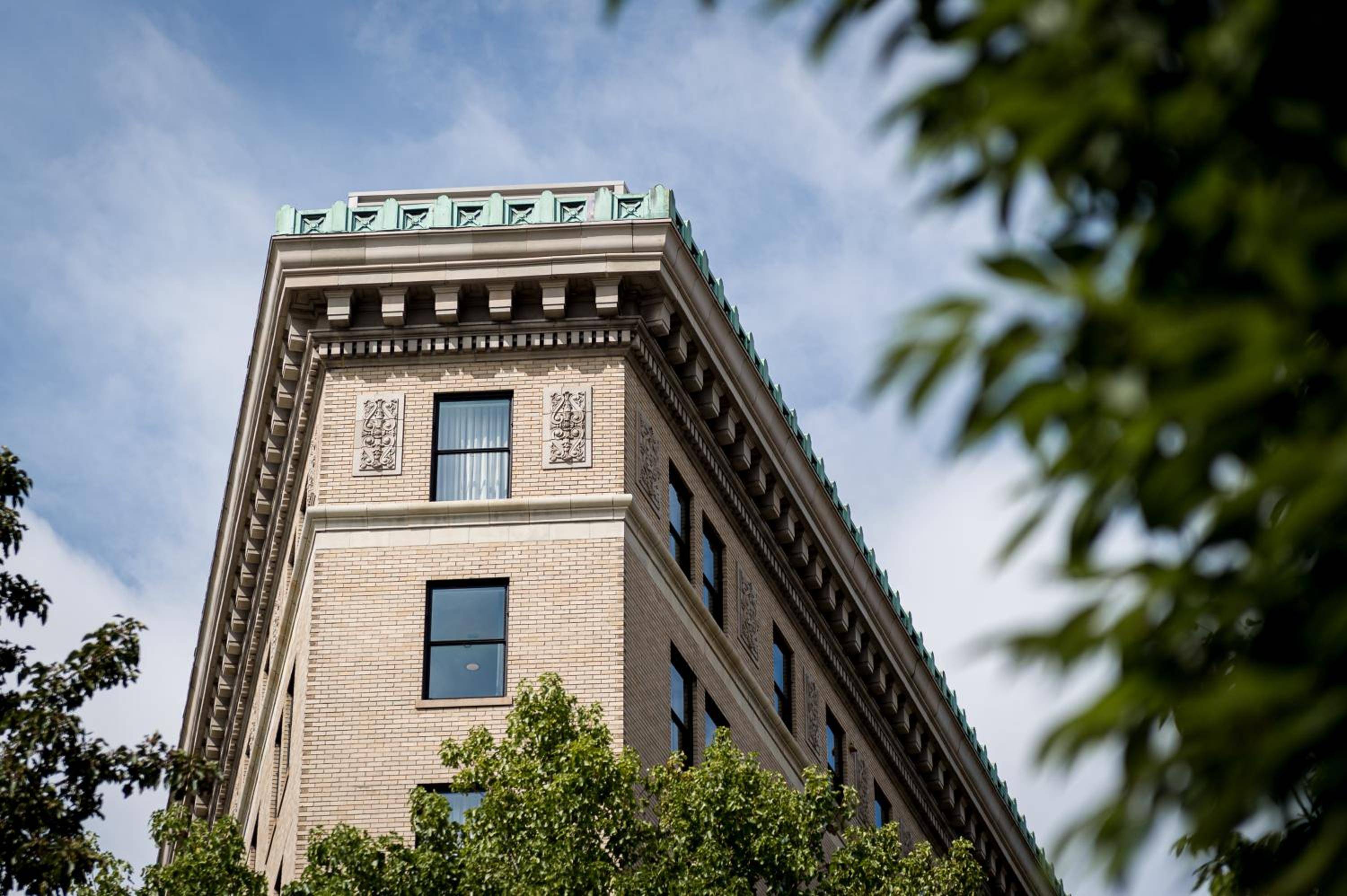 Ornate terra cotta panels and classical cornices crown this striking brick facade, where historic grandeur meets modern hospitality beneath a canopy of leafy branches.