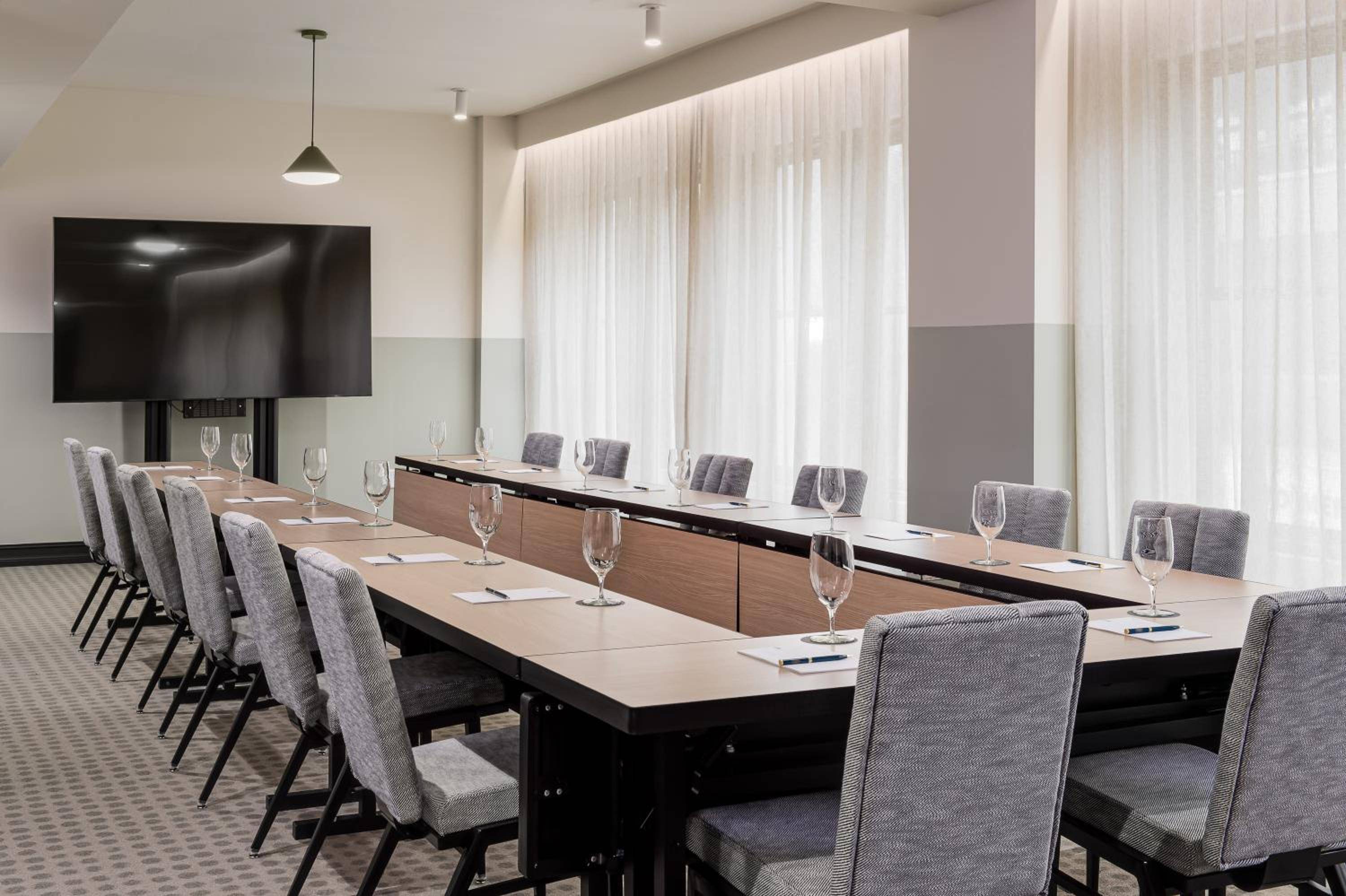 Sophisticated boardroom blends warm wood with contemporary gray upholstery, where floor-to-ceiling curtains filter natural light across the polished conference table.