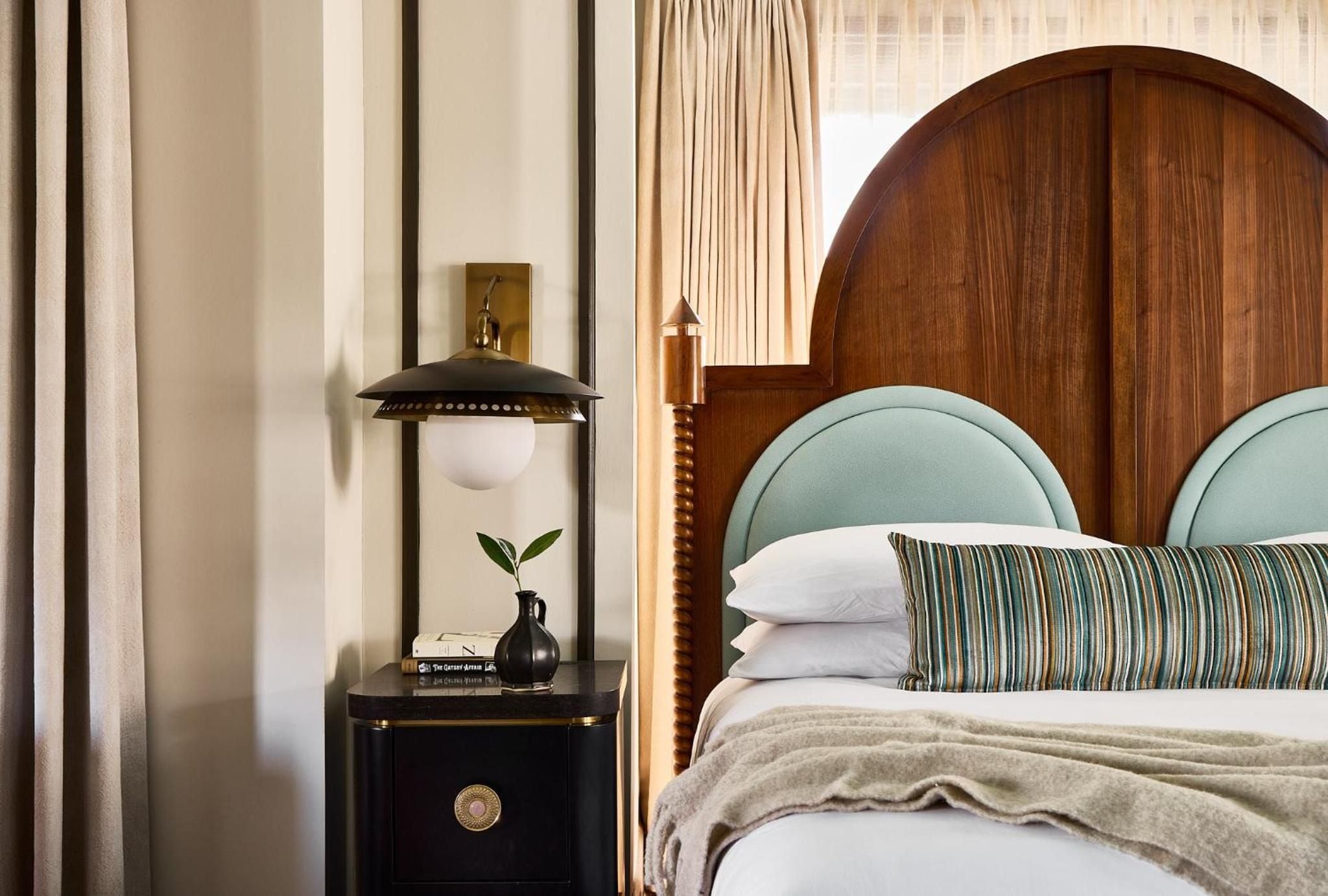 Warm wood headboards frame sage-green upholstery while brass-detailed nightstands hold vintage-inspired lamps, creating an intimate sanctuary bathed in golden afternoon light.