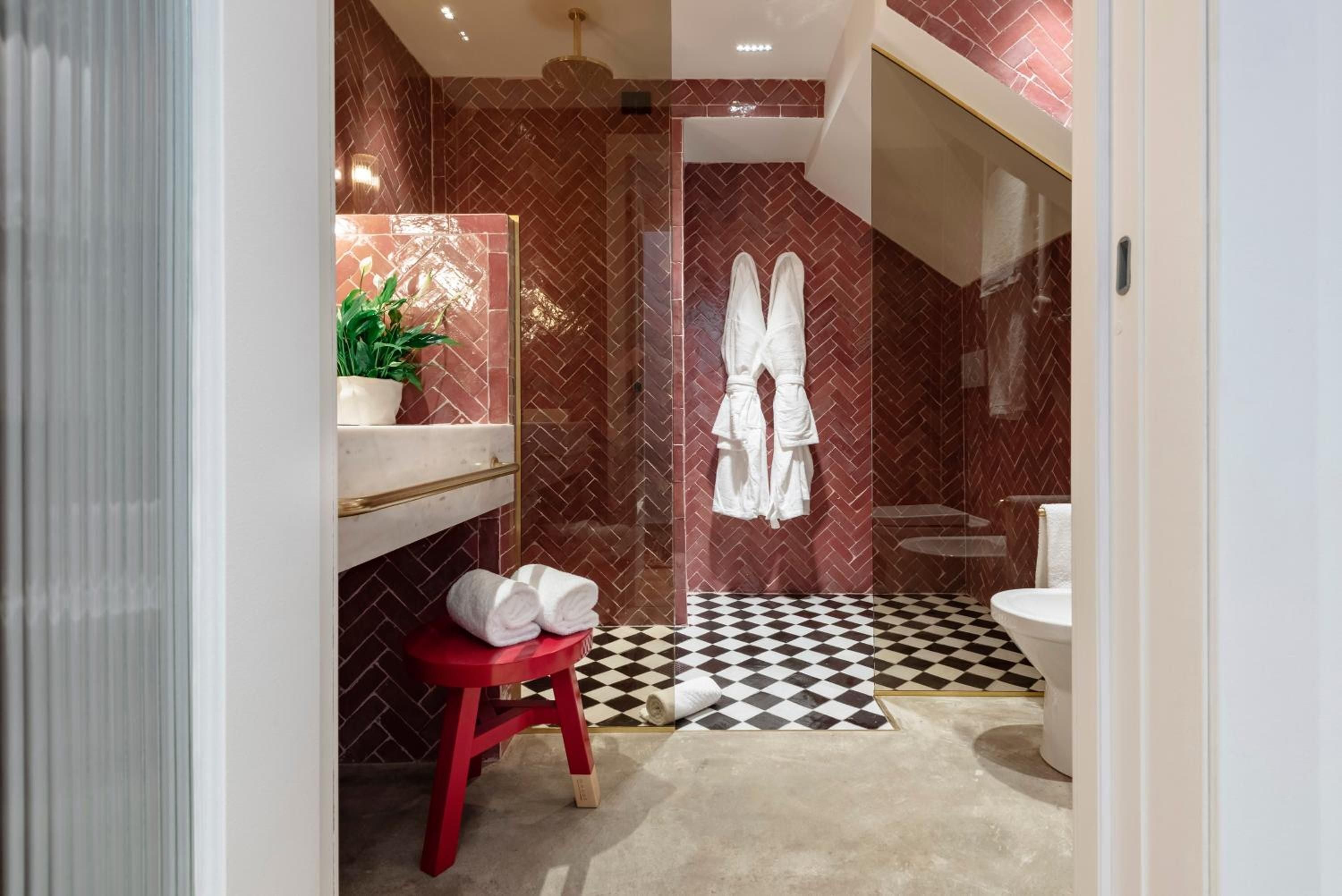 Burgundy herringbone tiles create intimate warmth in this sophisticated bathroom, where checkered floors and brass accents deliver playful Milan design sensibility.