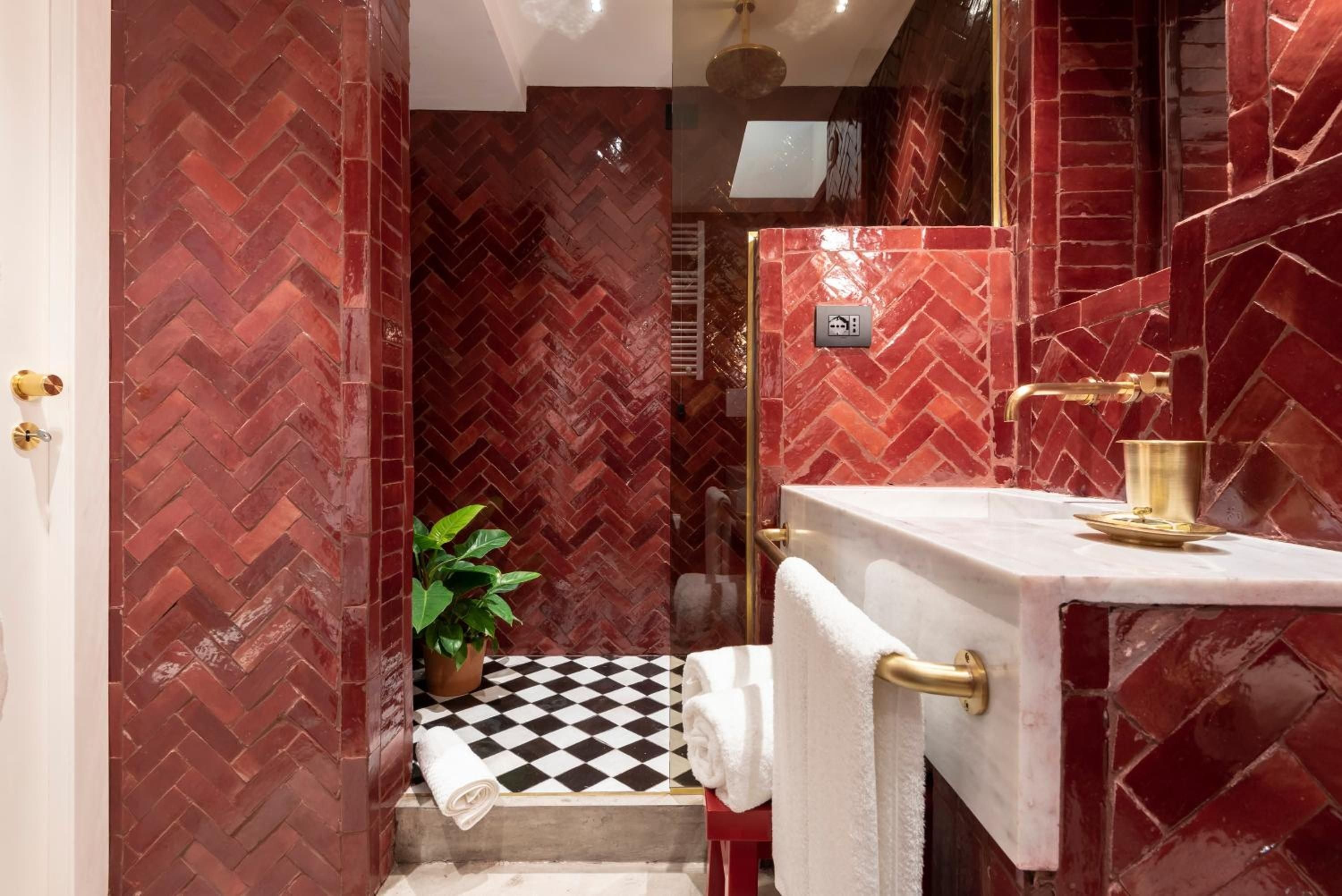 Rich burgundy zellige tiles in herringbone patterns create an intimate jewel box bathroom, where brass fixtures gleam against marble surfaces and checkered floors add playful contrast.