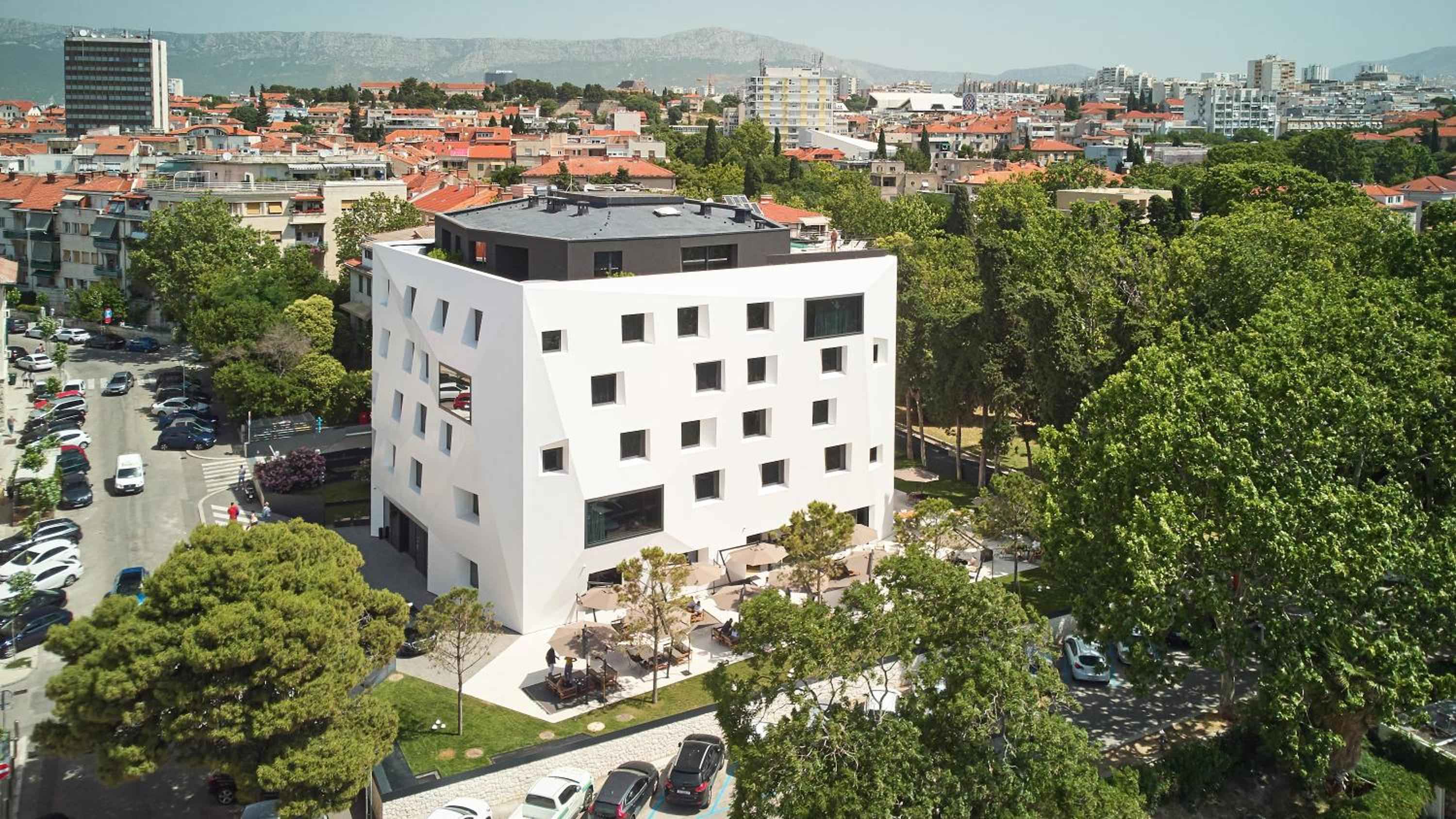Striking white geometric facade rises like a modern sculpture above Split's terracotta rooftops, its scattered windows creating dramatic shadows against the Mediterranean light.