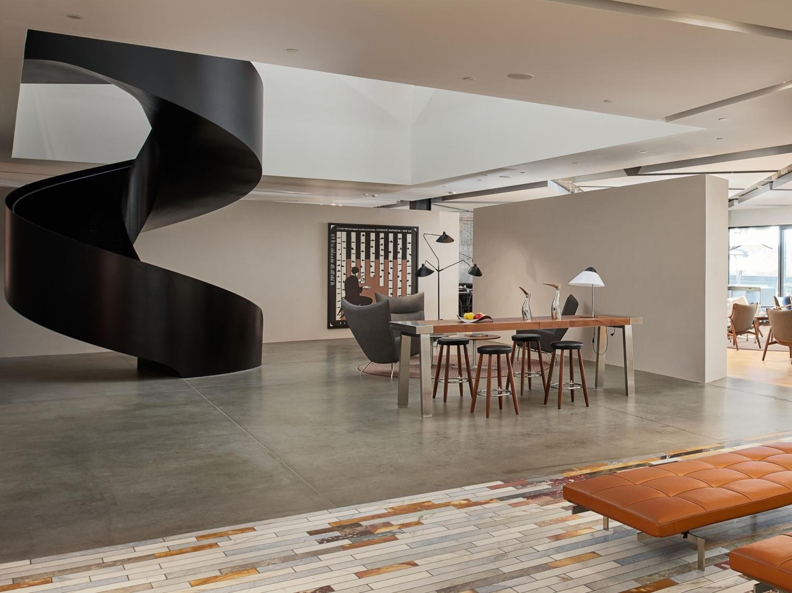 A sculptural black spiral staircase commands attention in this sophisticated common area, where polished concrete floors meet warm wood furnishings and modern lighting creates intimate gathering spaces.