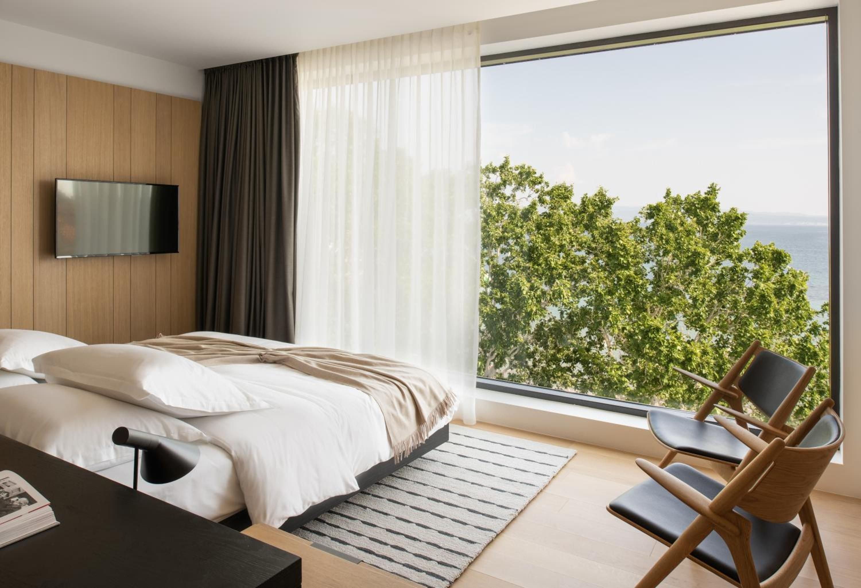 Floor-to-ceiling windows frame verdant treetops while warm wood paneling and crisp linens create a serene sanctuary where modern minimalism meets natural beauty.