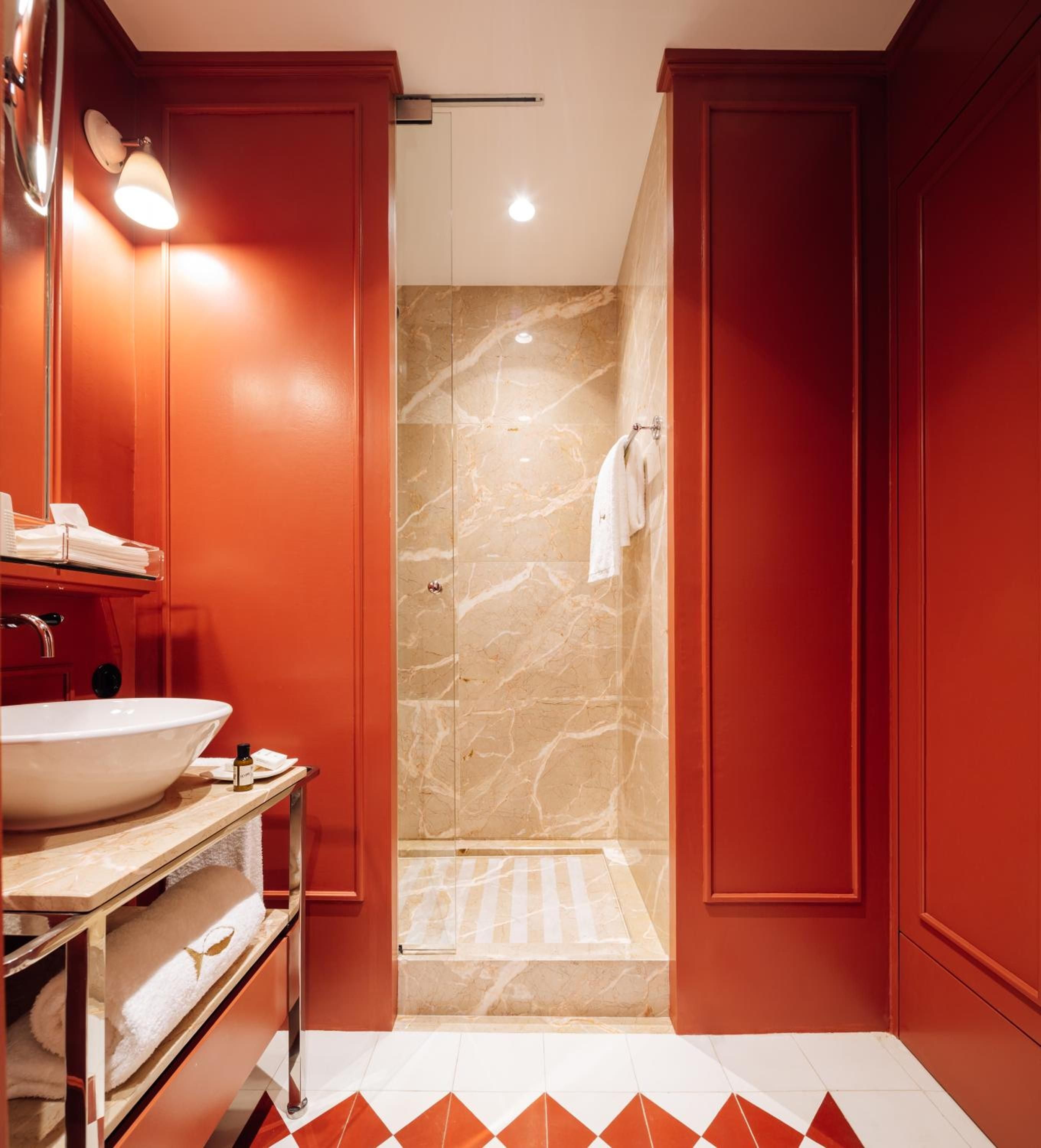 Bold terracotta walls embrace marble surfaces in this jewel-box bathroom, where warm lighting and geometric floor tiles create an intimate, sophisticated retreat.