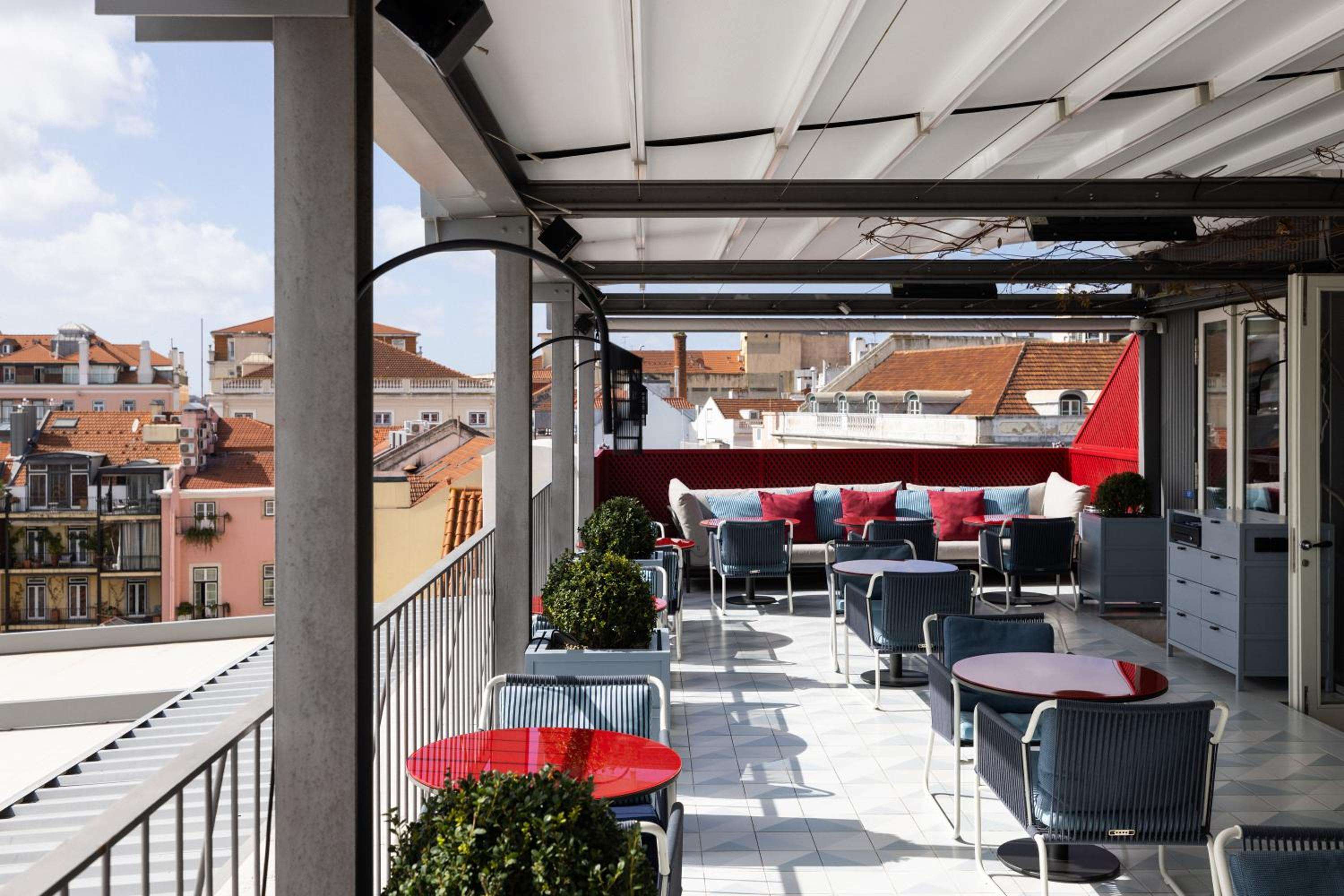 Modern wicker seating and crimson accent tables create intimate gathering spots on this airy rooftop terrace, where Lisbon's terracotta rooftops unfold in panoramic splendor.