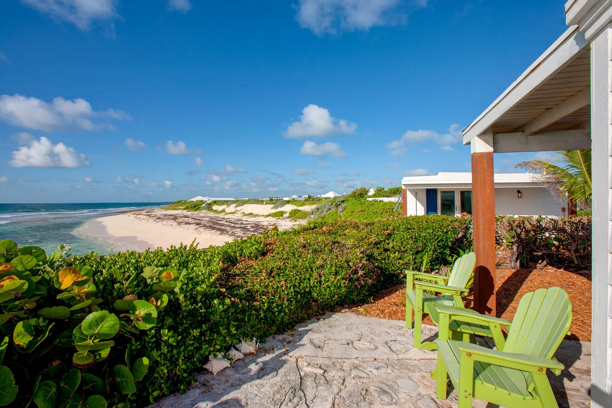 Lime-green Adirondack chairs frame pristine Elbow Cay shoreline, where native sea grape hedges meet powder-soft sand and crystalline Bahamian waters stretch toward the horizon.