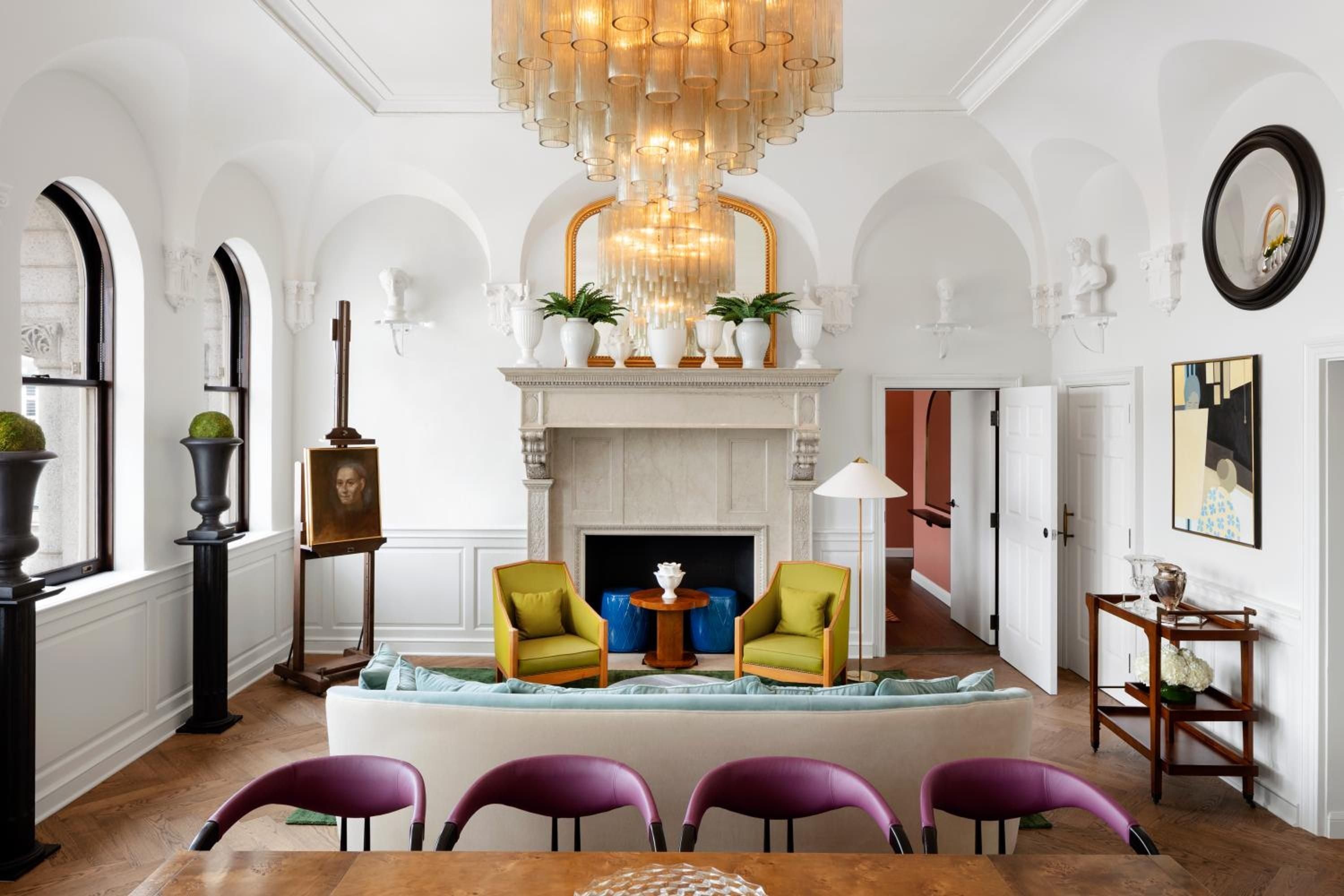 Jewel-toned chairs ring the mahogany dining table while chartreuse armchairs anchor the sitting area beneath cascading amber glass chandeliers in this elegant salon.