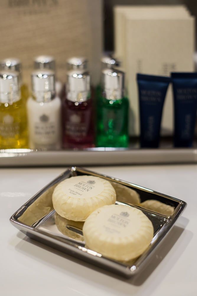 Premium toiletries and handcrafted soaps rest in polished chrome, while jewel-toned bottles catch natural light on marble surfaces—luxury in every thoughtful detail.