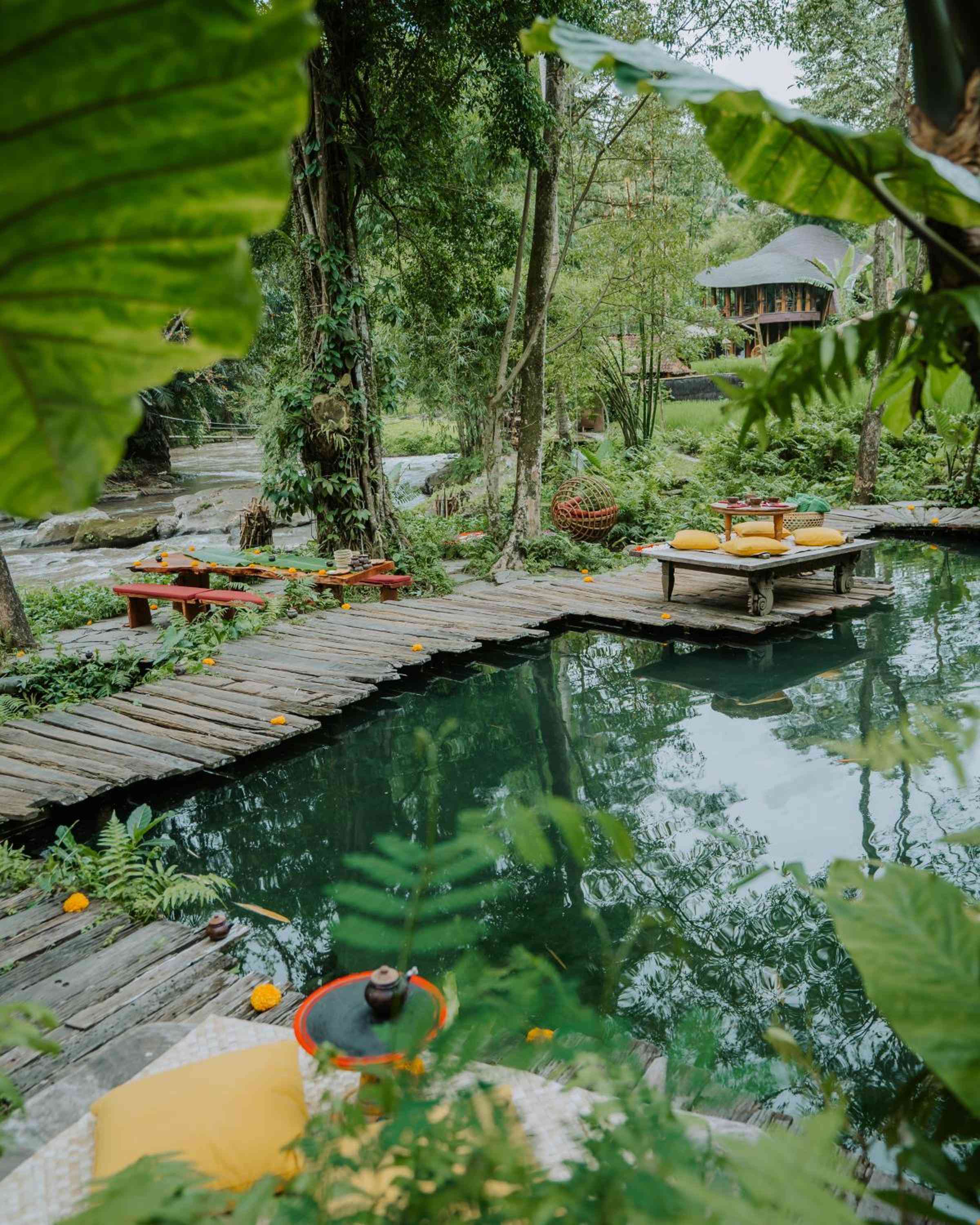 Weathered wooden platforms float above emerald spring waters, where floating tea ceremonies unfold beneath swaying palms and ancient trees in this enchanted Balinese sanctuary.