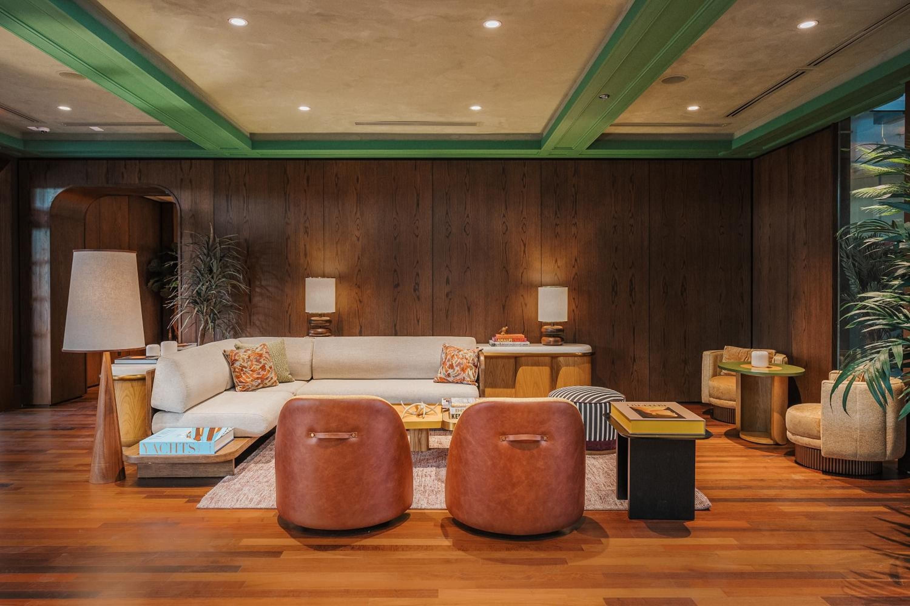 Warm wood paneling and emerald ceiling beams frame plush seating areas where cognac leather ottomans invite lingering conversations over coffee and magazines.