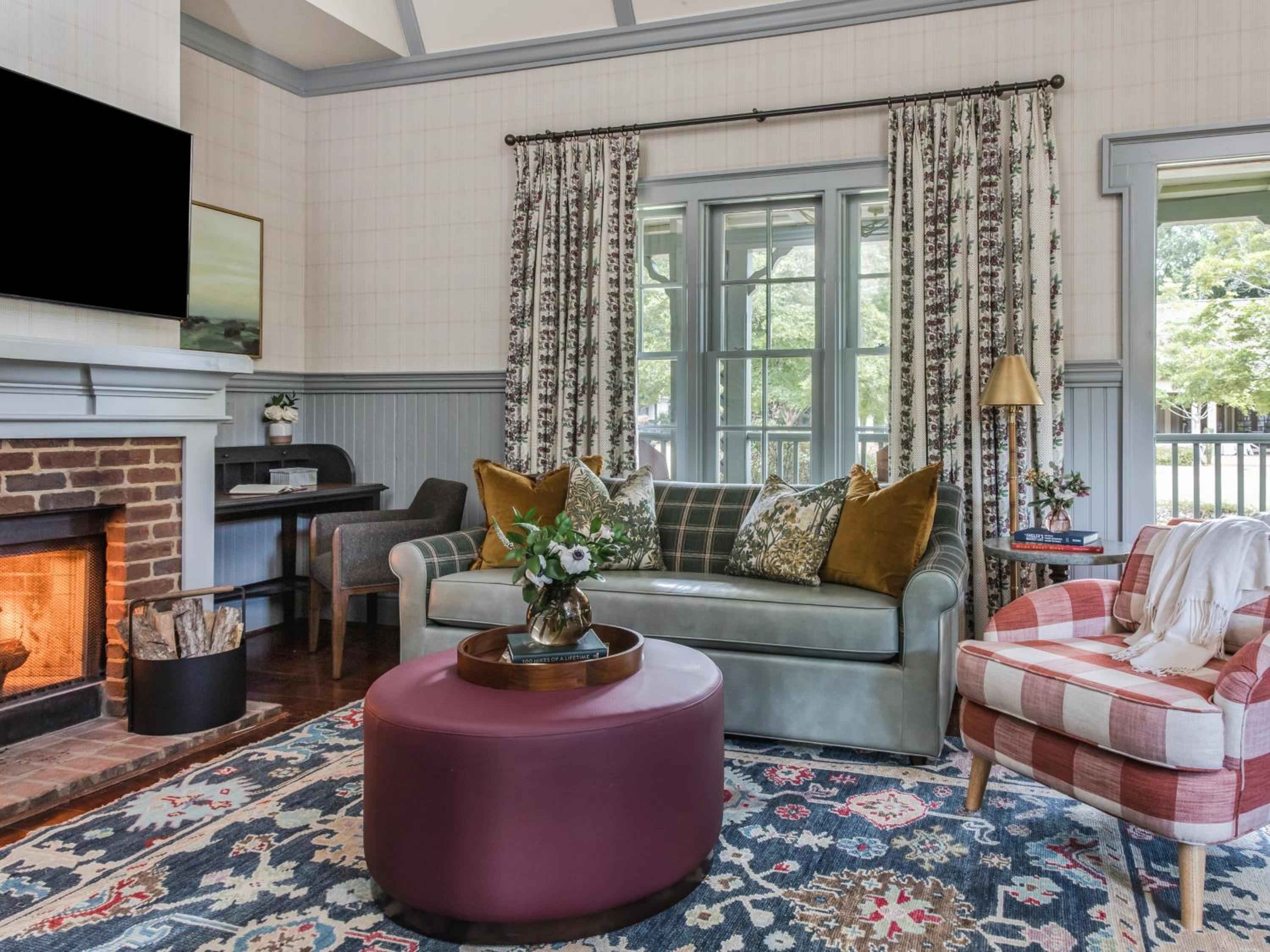 Plaid cushions and botanical prints create cottage charm in this inviting sitting area, where crackling firelight dances across polished hardwood floors and jewel-toned furnishings.