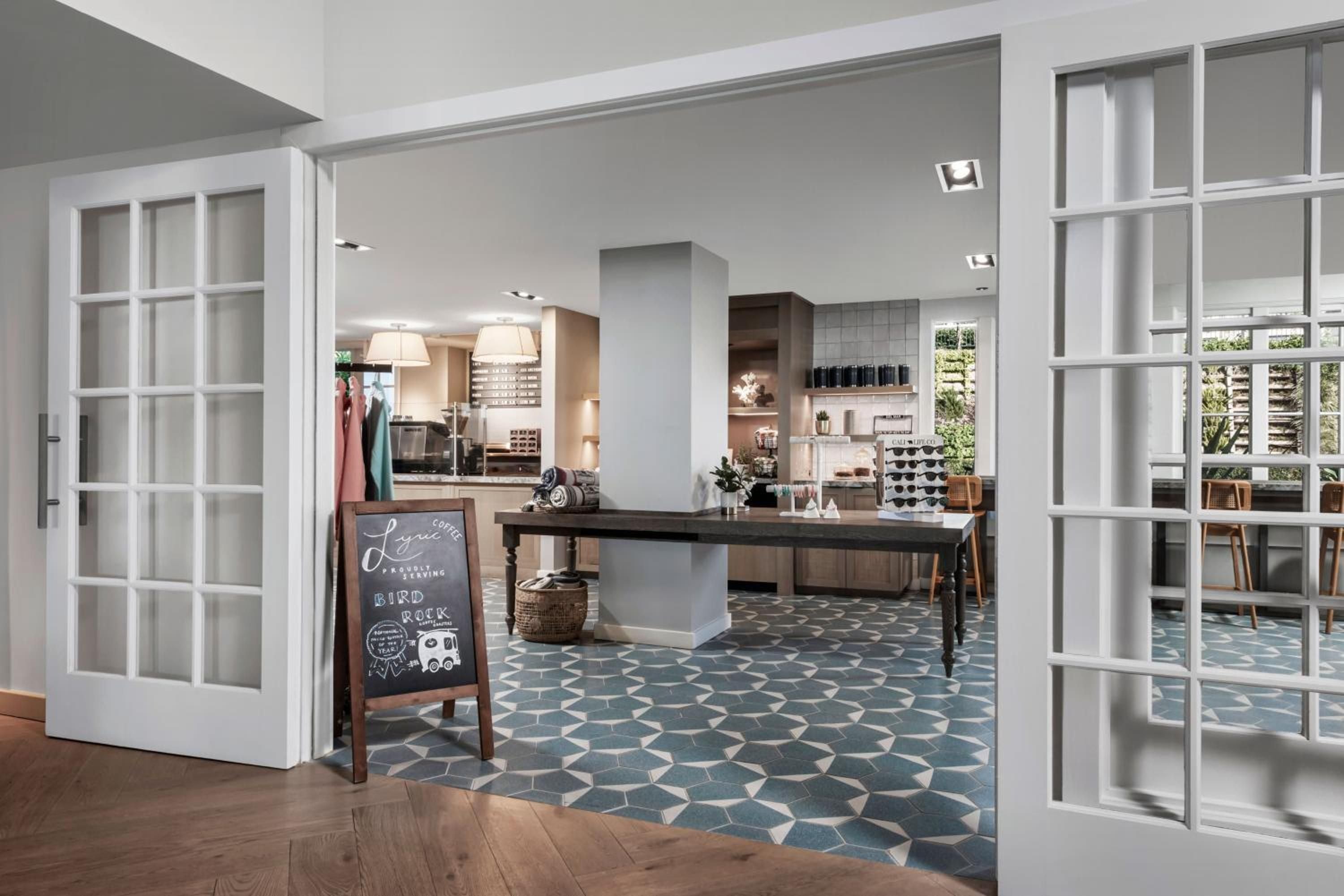 French doors open onto a sophisticated retail space where geometric blue tiles meet warm wood, creating an inviting boutique atmosphere with artisanal touches and coastal elegance.