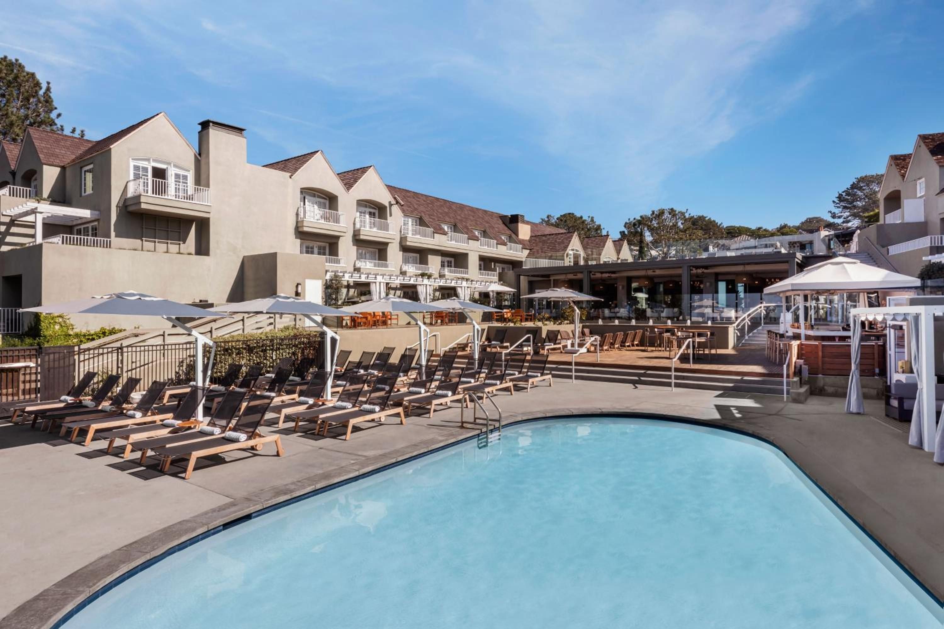 Sleek loungers ring the curved pool where Mediterranean-inspired architecture meets California sunshine, creating an intimate resort oasis beneath azure skies.