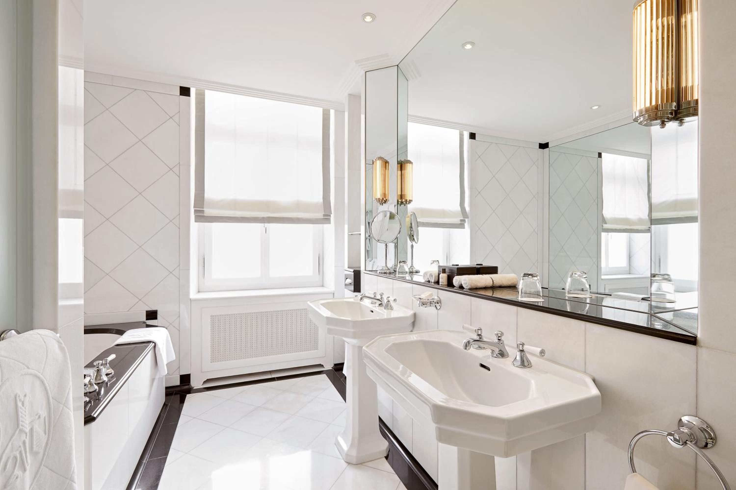 Pristine white marble surfaces and gleaming chrome fixtures create a spa-like sanctuary, where herringbone tile patterns and golden pendant lights add architectural sophistication to the luxurious bathing ritual.