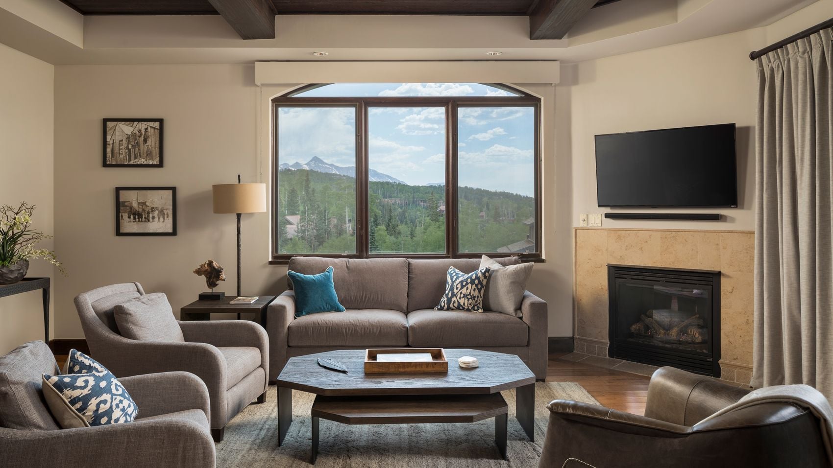 Mountain vistas frame plush gray seating and exposed timber beams, where crackling firelight mingles with alpine air through floor-to-ceiling windows.
