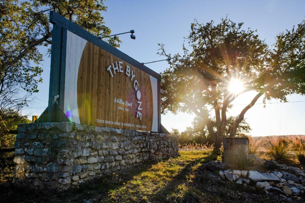 Golden hour light filters through ancient oaks, illuminating the stone-and-timber entrance sign that welcomes guests to this Hill Country retreat.