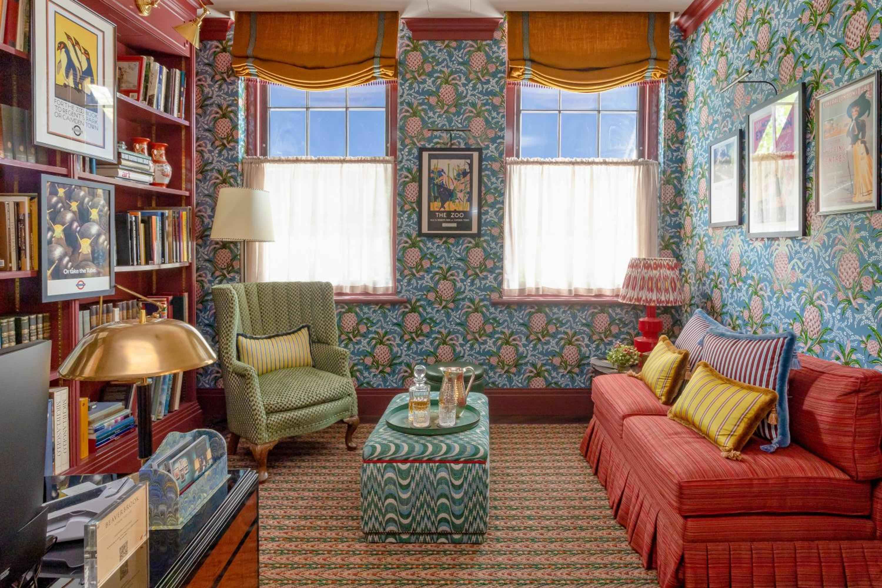 Vibrant pineapple wallpaper and coral-hued seating create an exuberantly English library, where golden afternoon light filters through café curtains onto well-thumbed books and vintage travel posters.