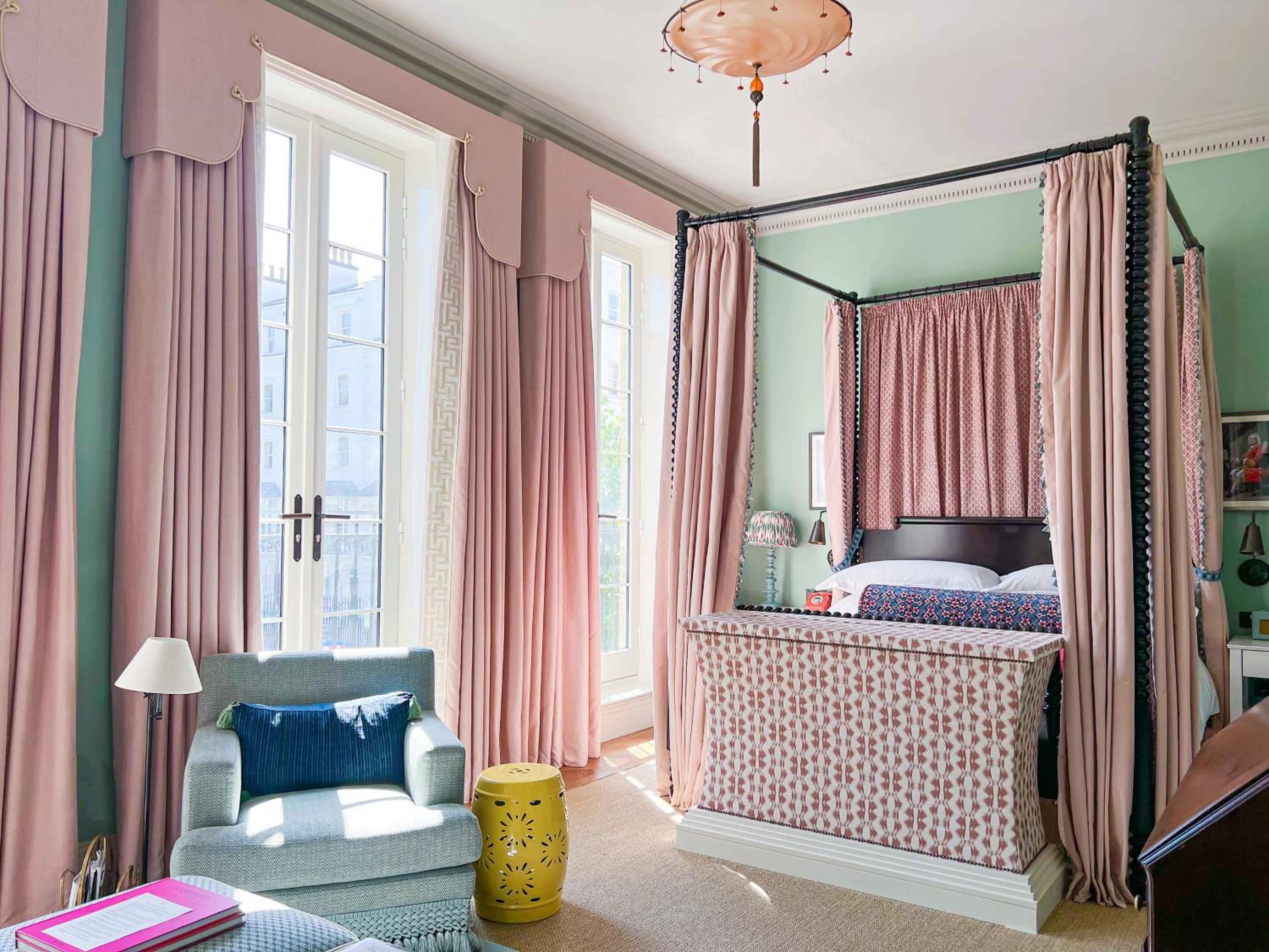 Pink silk curtains frame tall windows while a four-poster bed draped in coral patterns creates an intimate cocoon within mint-green walls.