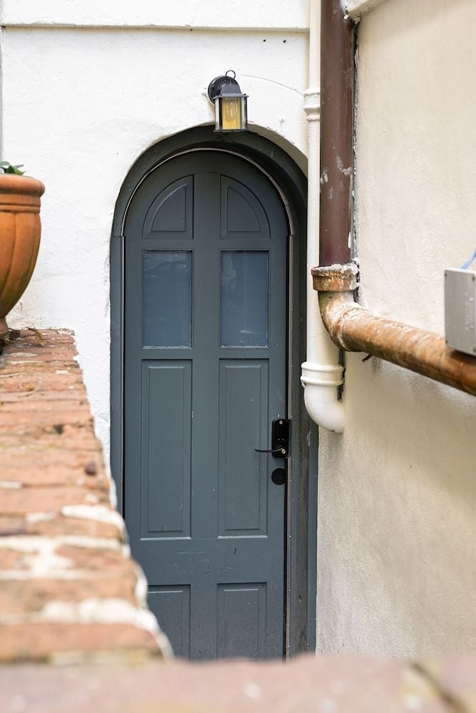 Weathered brick steps lead to an arched doorway painted in deep sage, where a glowing lantern casts gentle shadows across textured stucco walls.