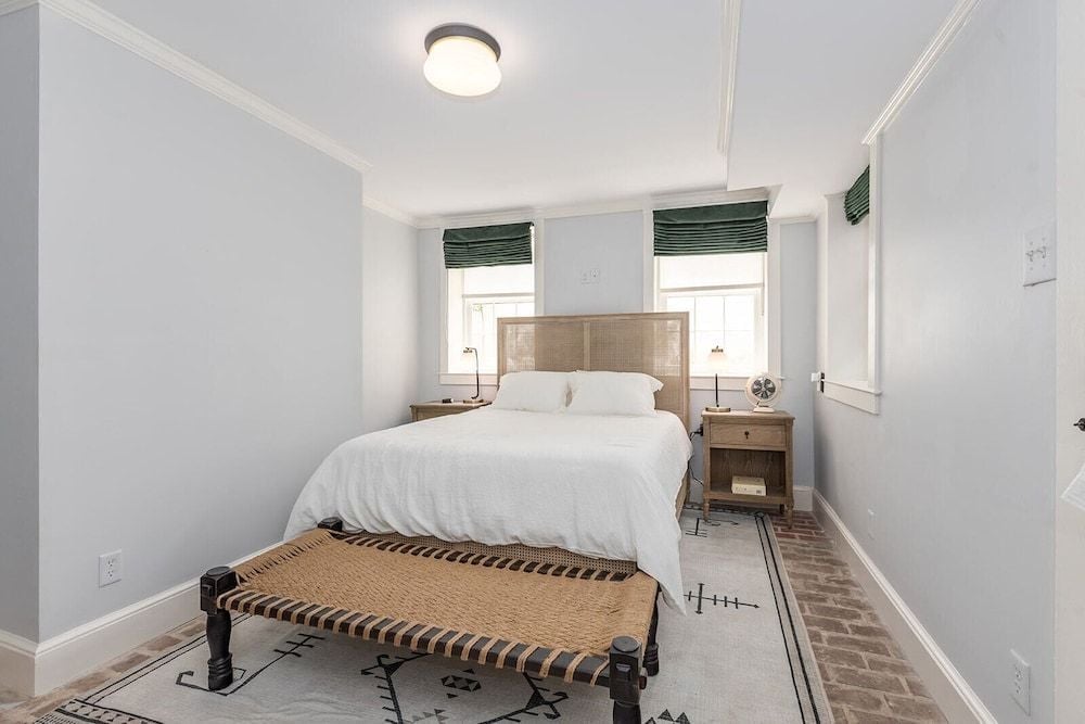 Woven cane headboards and brass pendant lights create intimate warmth in this thoughtfully appointed guest room, where natural textures meet crisp white linens.