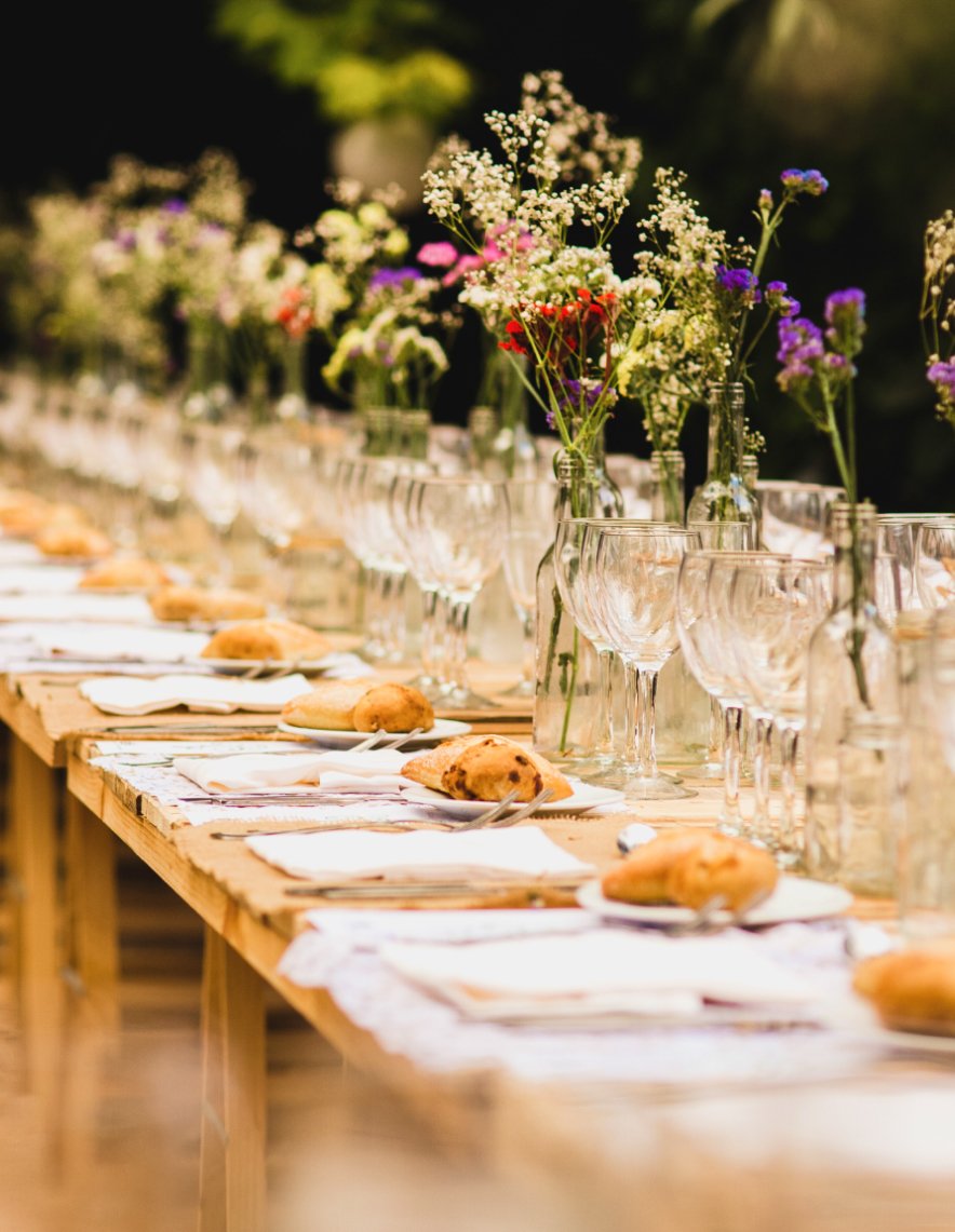 Rustic wooden tables showcase artisanal bread and wildflower arrangements in glass bottles, creating an intimate farm-to-table dining experience that celebrates local ingredients and natural beauty.