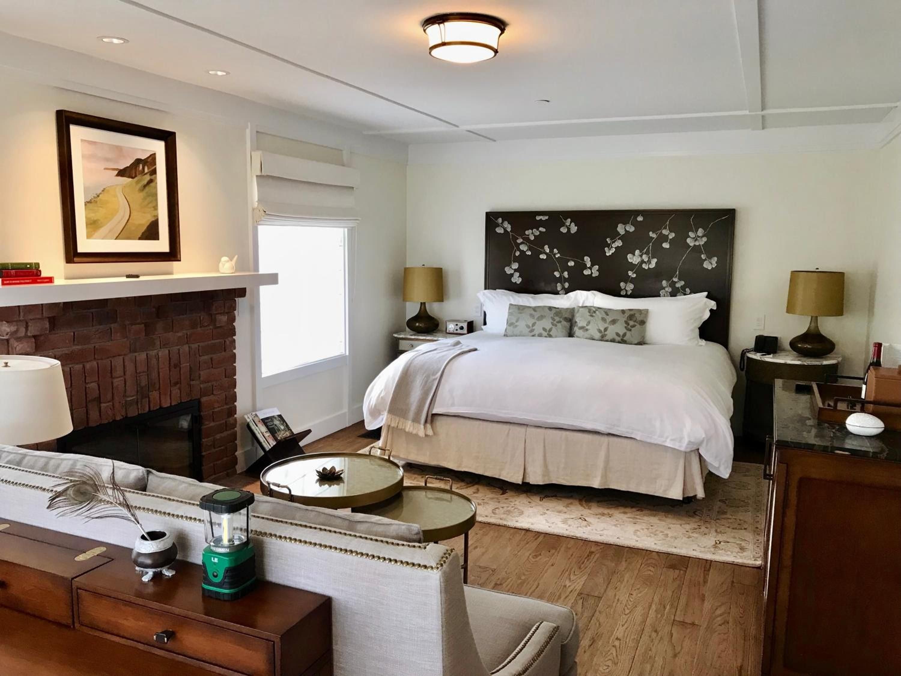 Exposed brick fireplace and botanical headboard art create intimate sophistication in this airy suite, where hardwood floors meet plush seating and thoughtful lighting design.