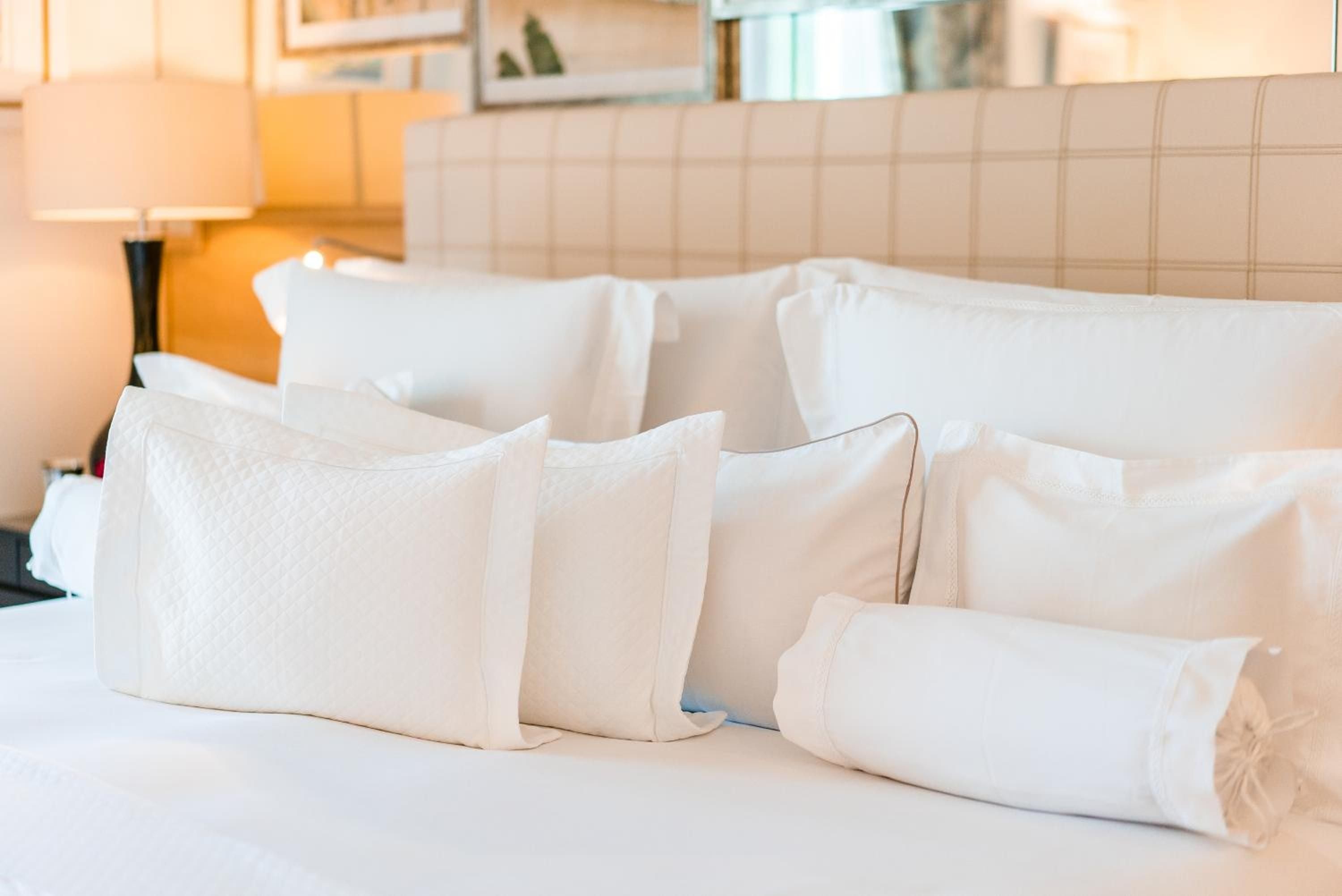 Crisp white linens and plump pillows create a cloud-like sanctuary, where afternoon light filters softly across the pristine bedding in this elegantly appointed guest room.