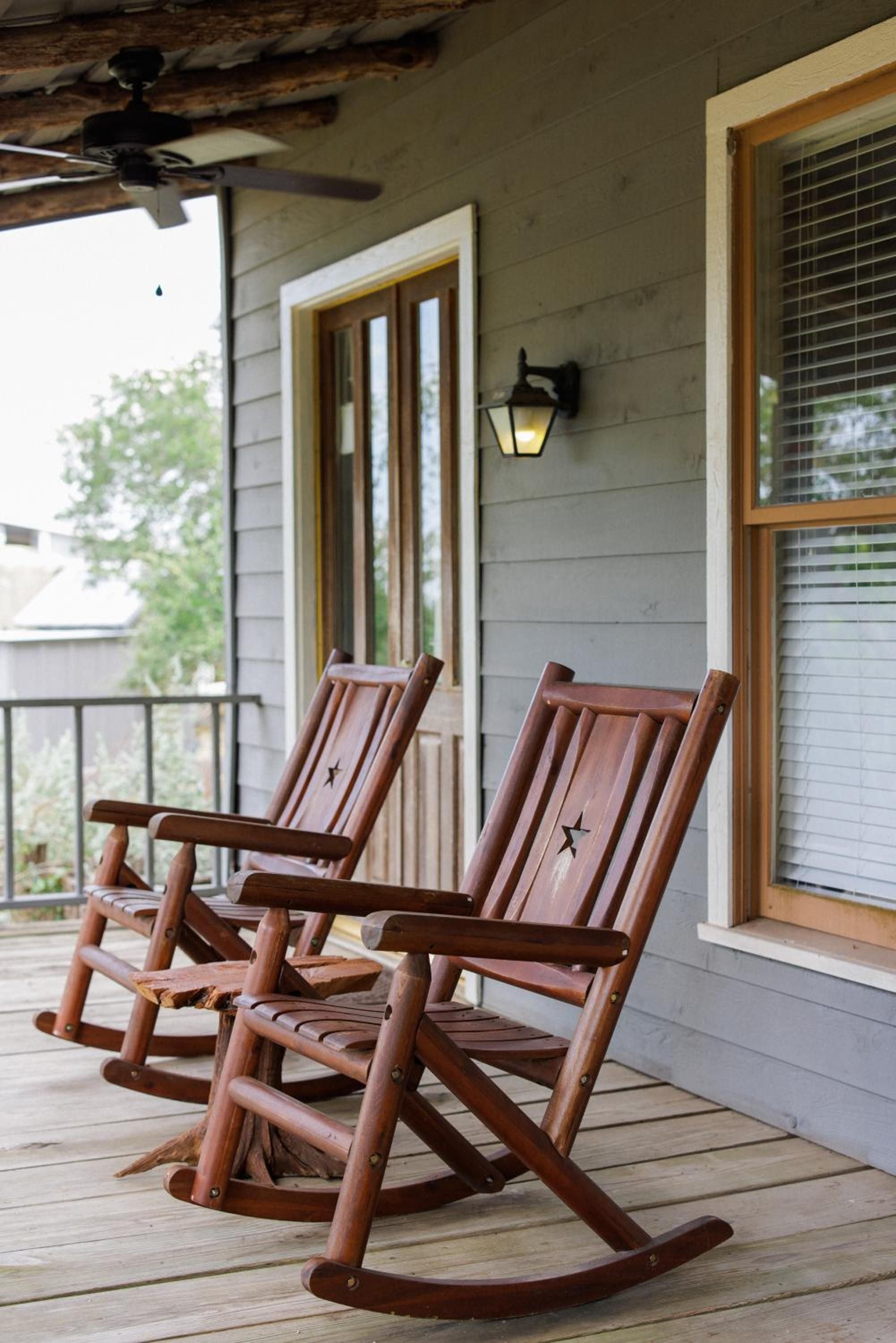 Hand-carved wooden rockers with rustic star details invite lingering conversations on the covered porch, where exposed beams and lantern light create an authentic Texas Hill Country sanctuary.