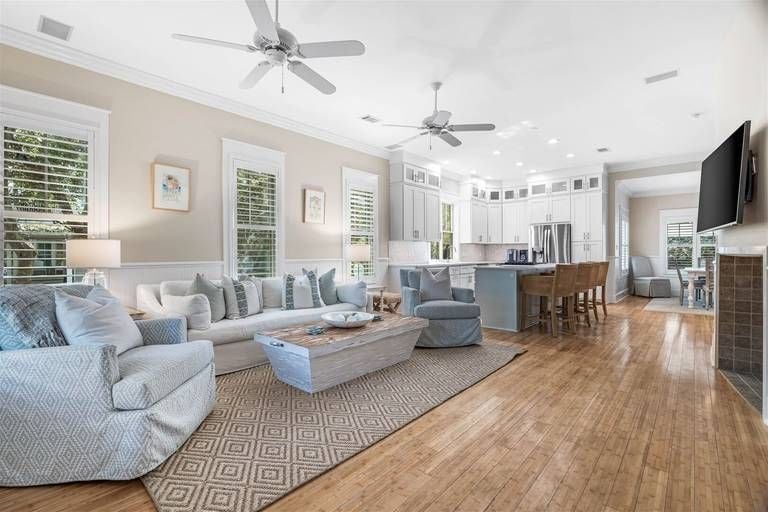 Open-concept living flows seamlessly into the gourmet kitchen, where soft gray sectionals and gleaming hardwood floors create an inviting coastal retreat.