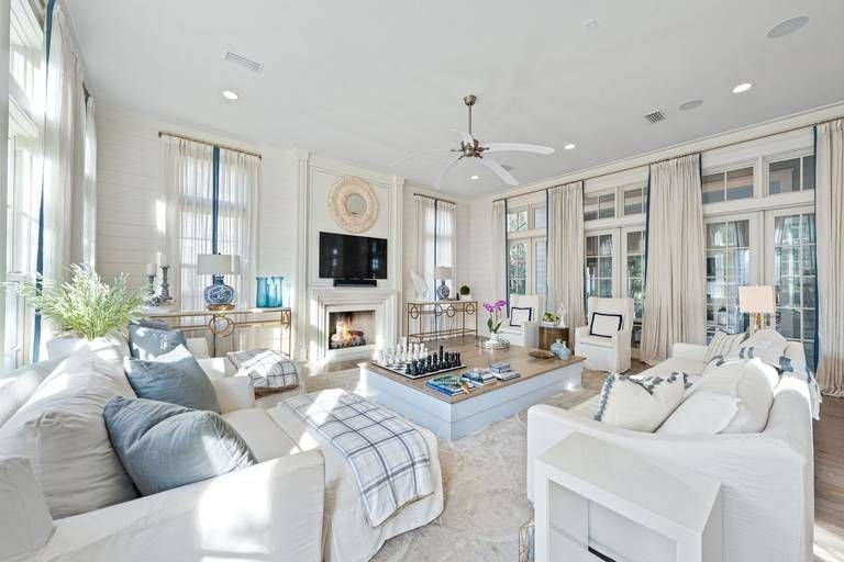 Soft morning light filters through floor-to-ceiling windows, illuminating this serene coastal living room where plaid throws and blue accents echo nearby ocean hues.