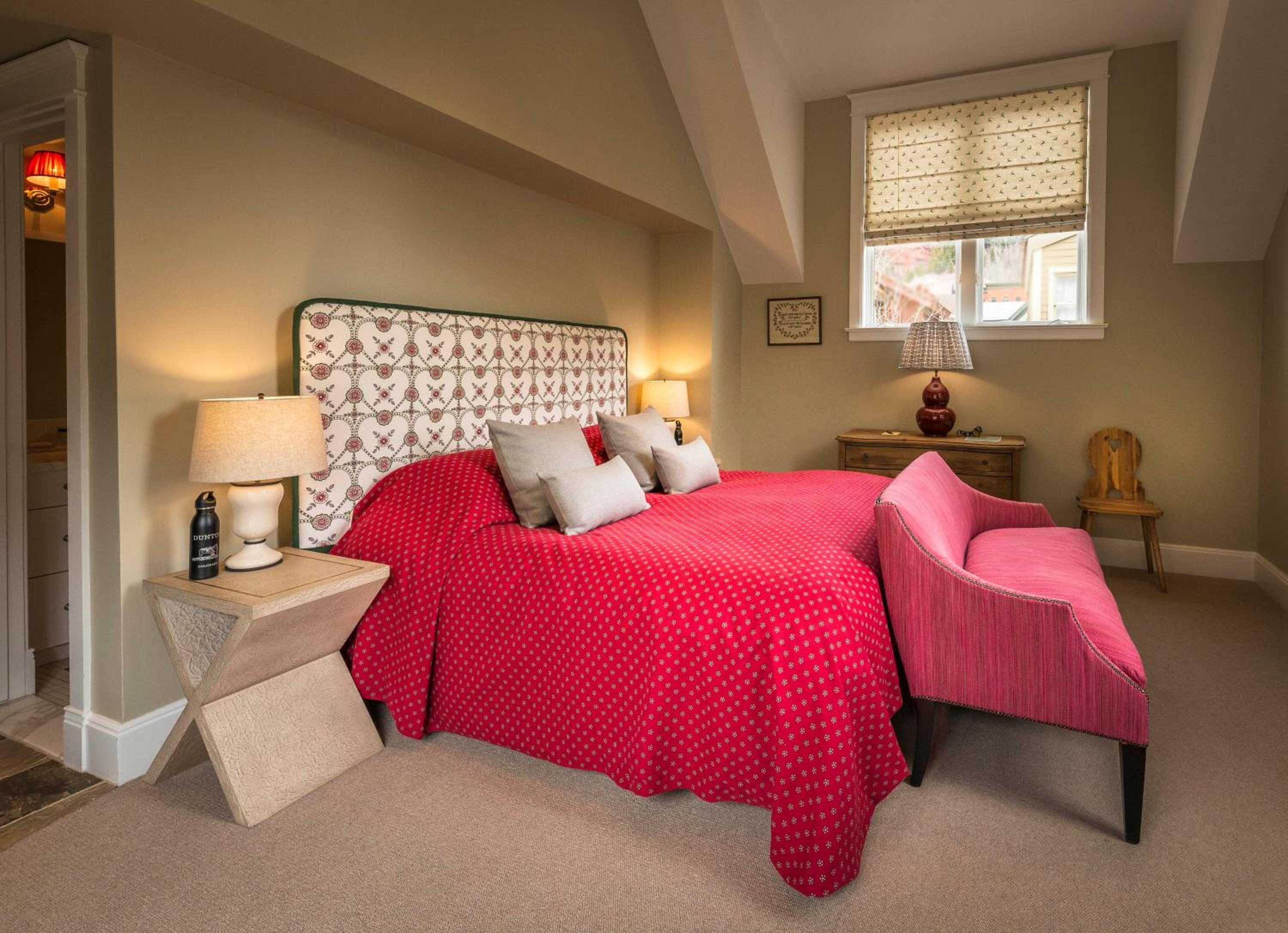 Exposed beams frame this intimate attic retreat where red polka-dot linens and patterned headboards create country charm beneath slanted eaves and honeyed light.