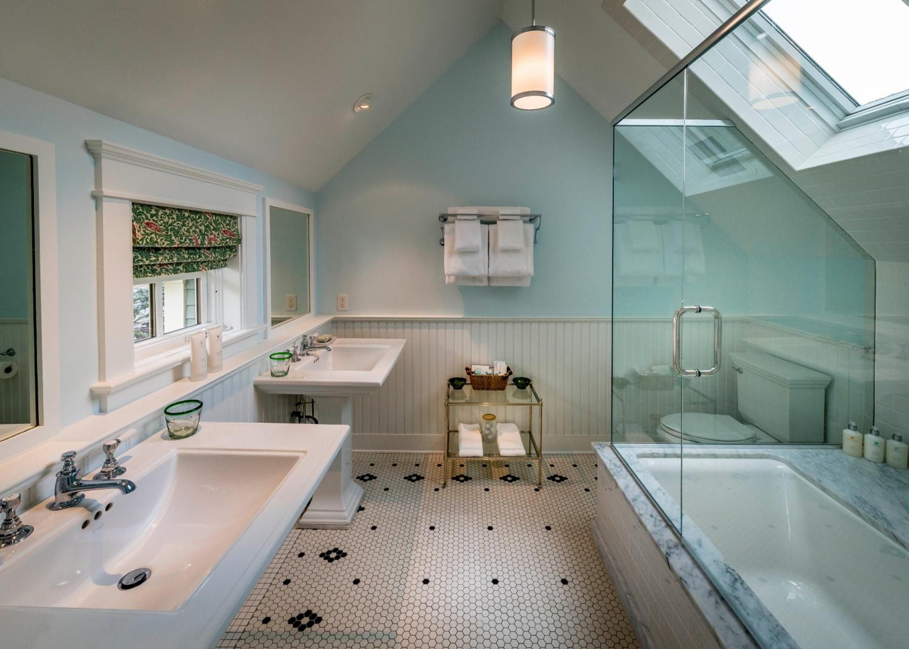 Hexagonal penny tiles and sage wainscoting create vintage charm in this skylit master bath, where marble counters and glass-enclosed shower exude timeless elegance.