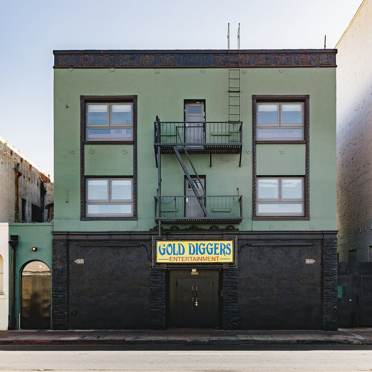 Mint-green facade and vintage fire escapes frame the unassuming entrance to this eclectic entertainment venue, where old-world charm meets contemporary hospitality on a quiet urban street.