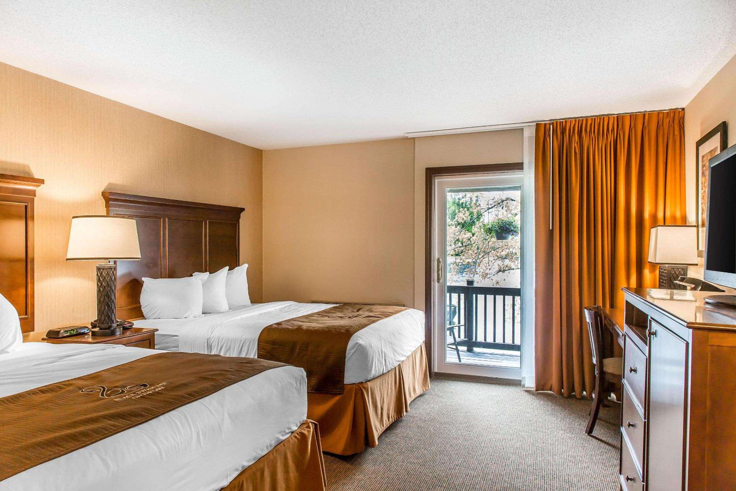 Warm amber drapes frame the balcony doors while rich mahogany headboards anchor crisp white linens in this inviting double-bed guest room.