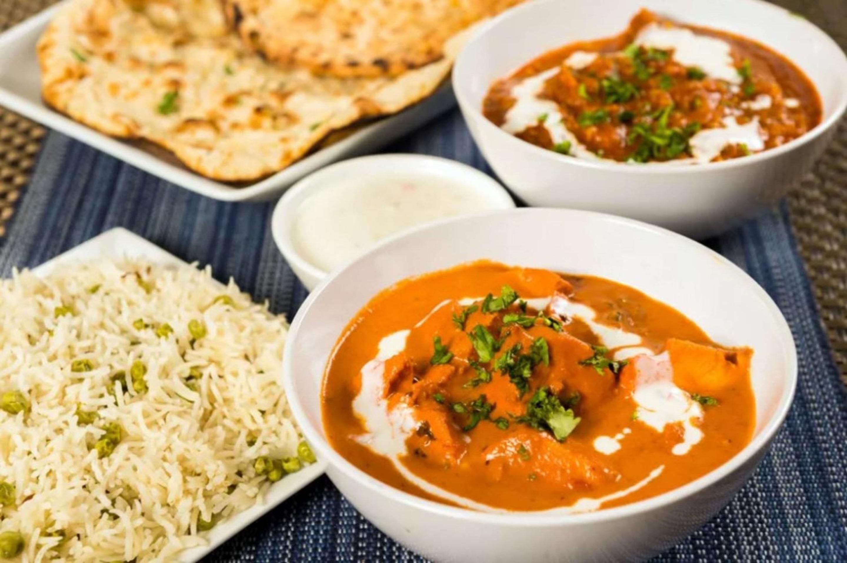 Fragrant Indian curries arrive with house-made naan and jeweled basmati rice, their vibrant orange hues brightened by delicate cream swirls and fresh cilantro.