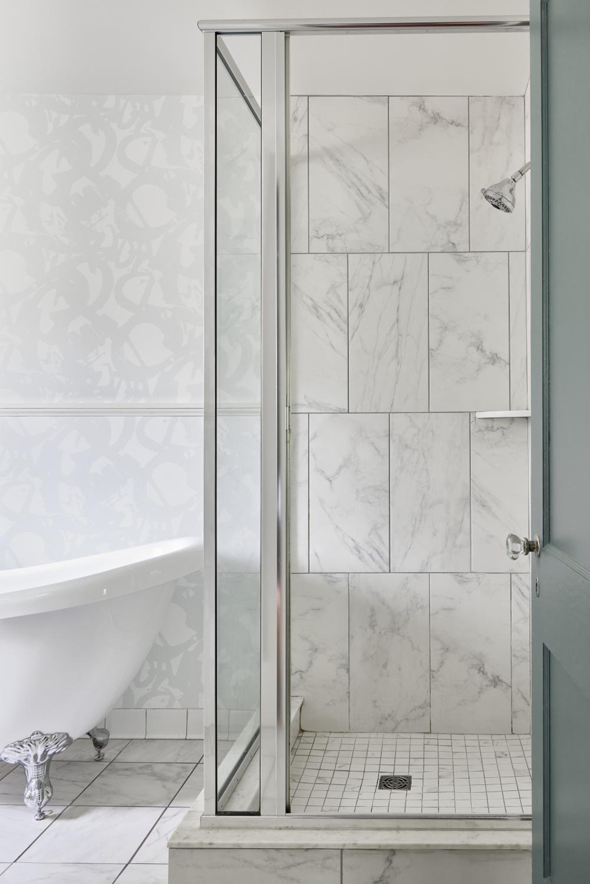 Carrara marble tiles create a serene backdrop in this spa-like bathroom, where natural light filters through glass to illuminate the elegant walk-in shower.