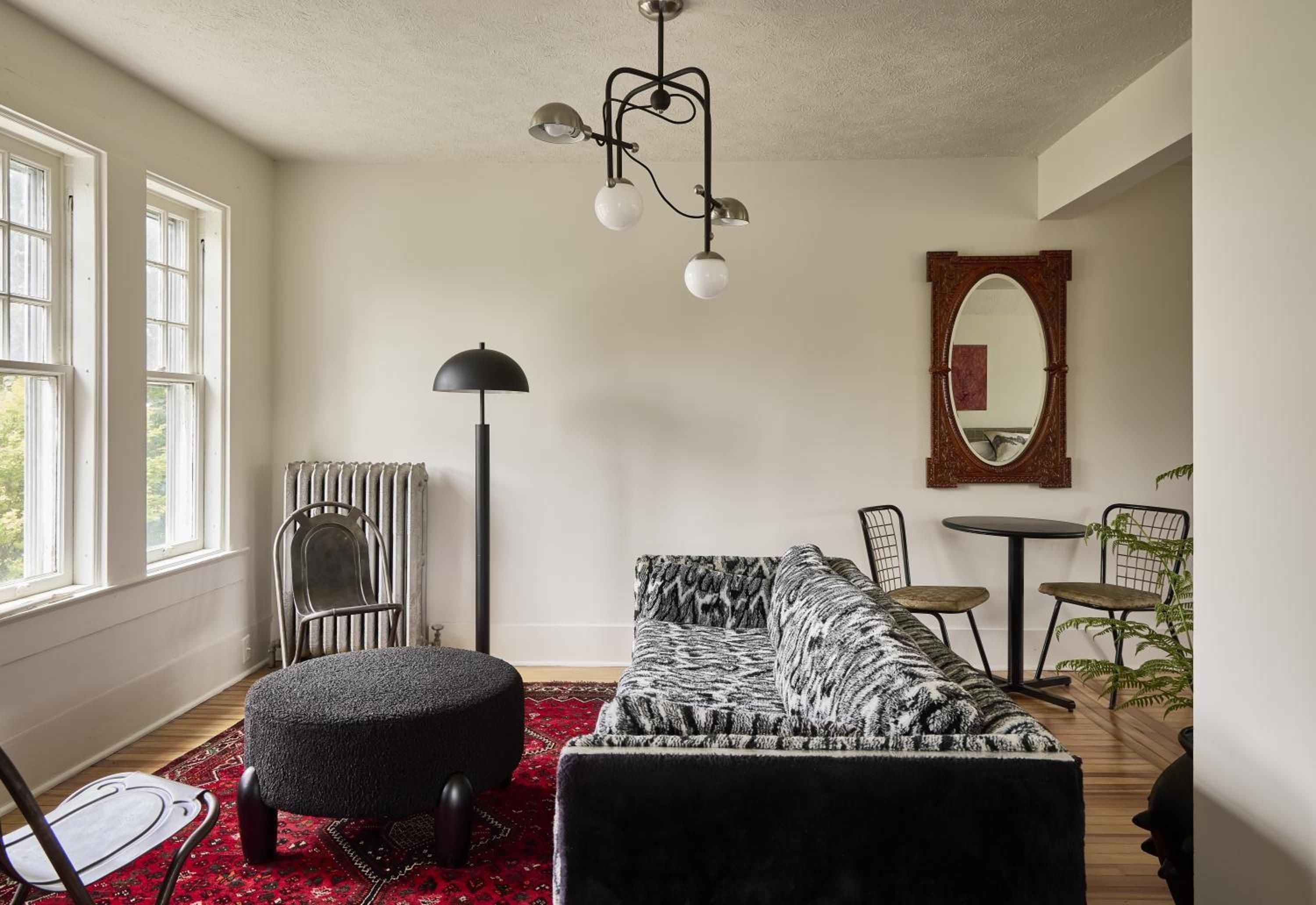 Sunlight streams through tall windows into this thoughtfully curated living space, where vintage radiators meet modern fixtures and a bold geometric sofa anchors the hardwood floors.