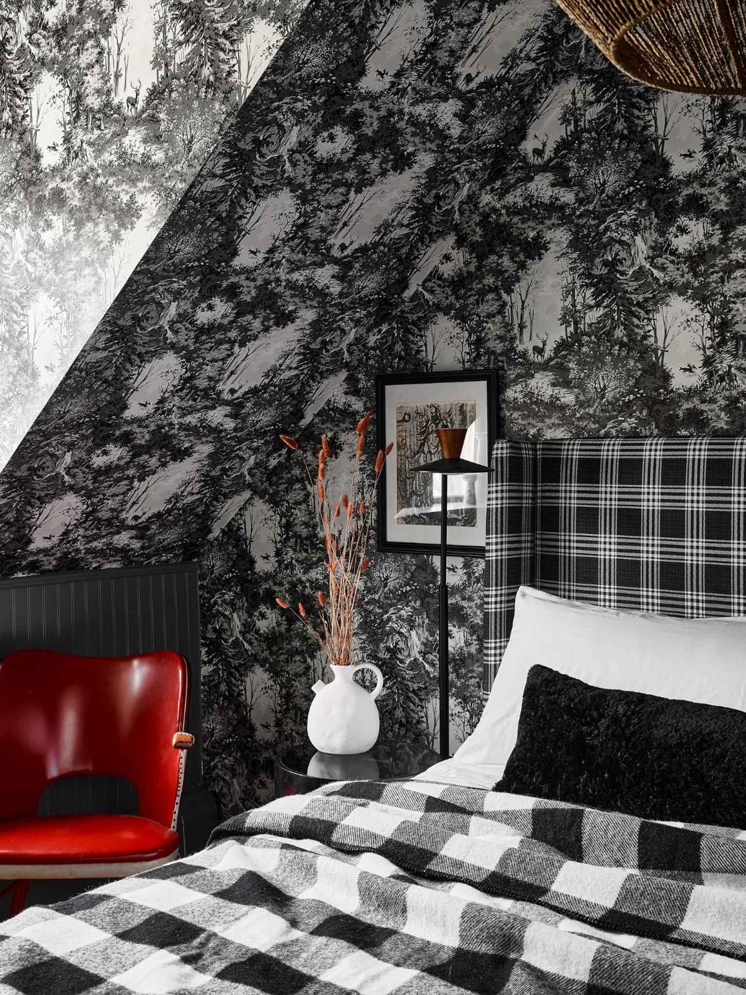 Dramatic botanical wallpaper transforms this attic bedroom into a moody retreat, where red leather mingles with plaid patterns beneath slanted ceilings.