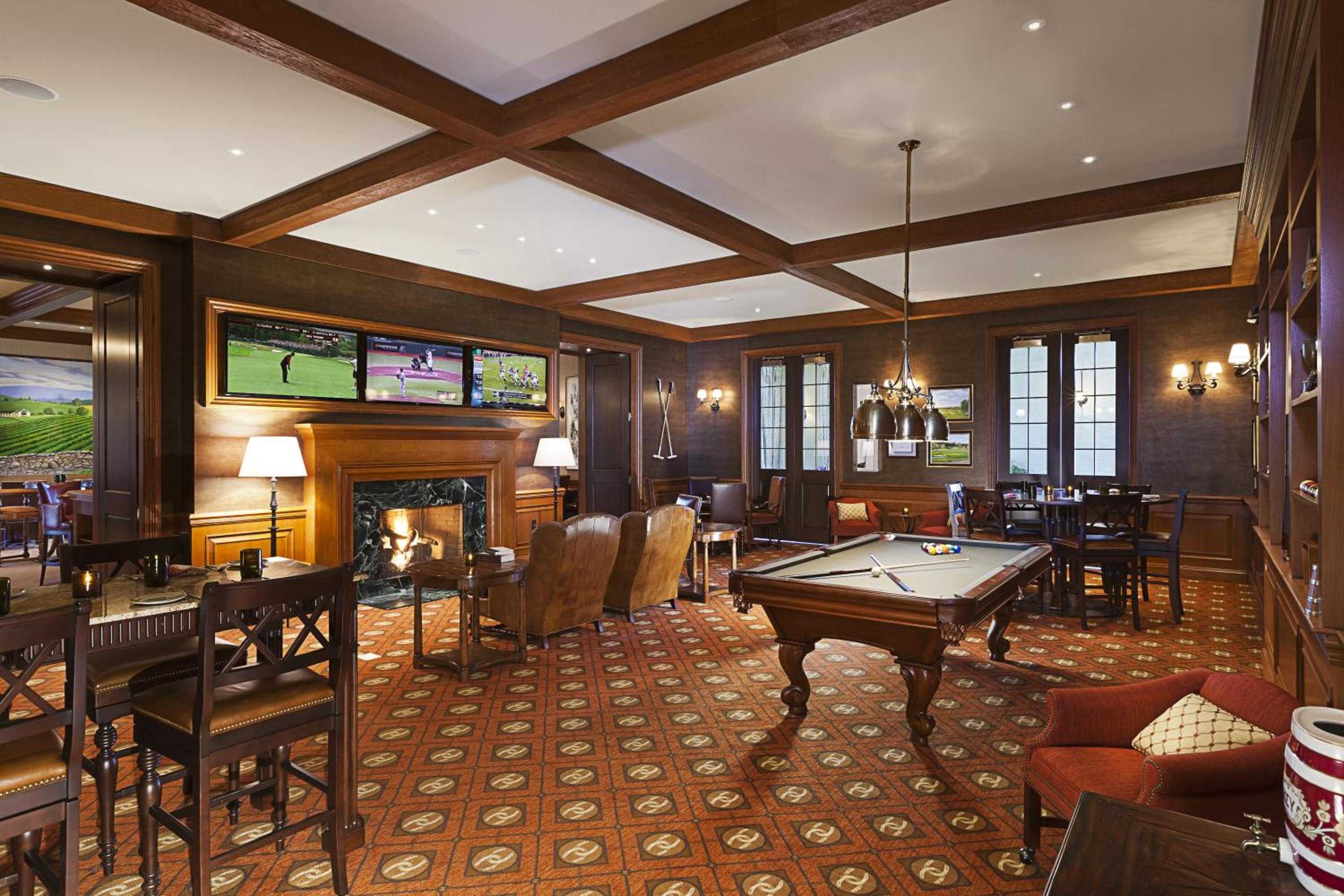 Rich mahogany paneling and coffered ceilings create an intimate gentleman's club atmosphere where billiards, multiple screens, and crackling fireplace invite lingering over evening cocktails.