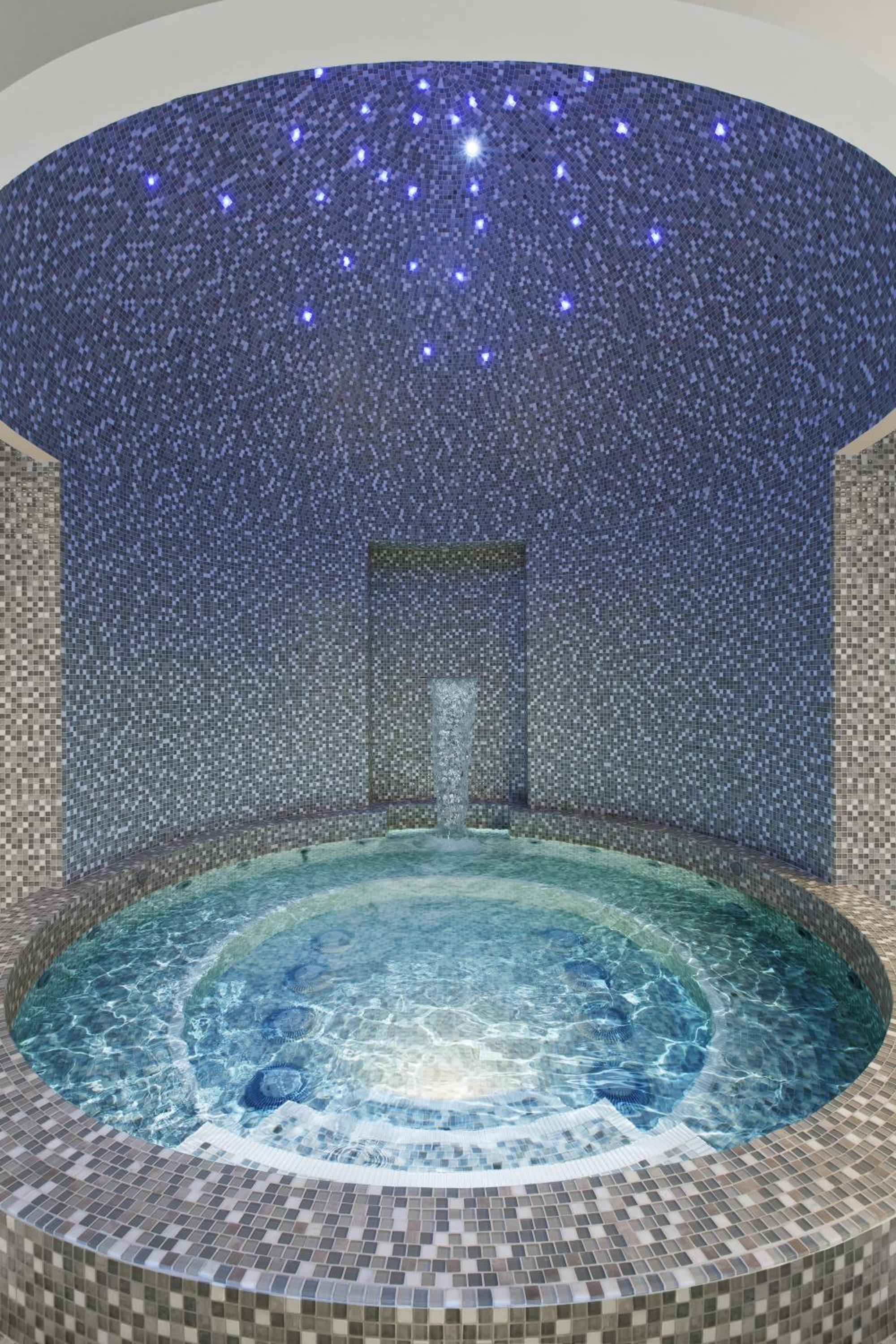 Fiber optic stars twinkle overhead in this intimate grotto spa, where mosaic tiles shimmer in blues and grays around a perfectly circular soaking pool.