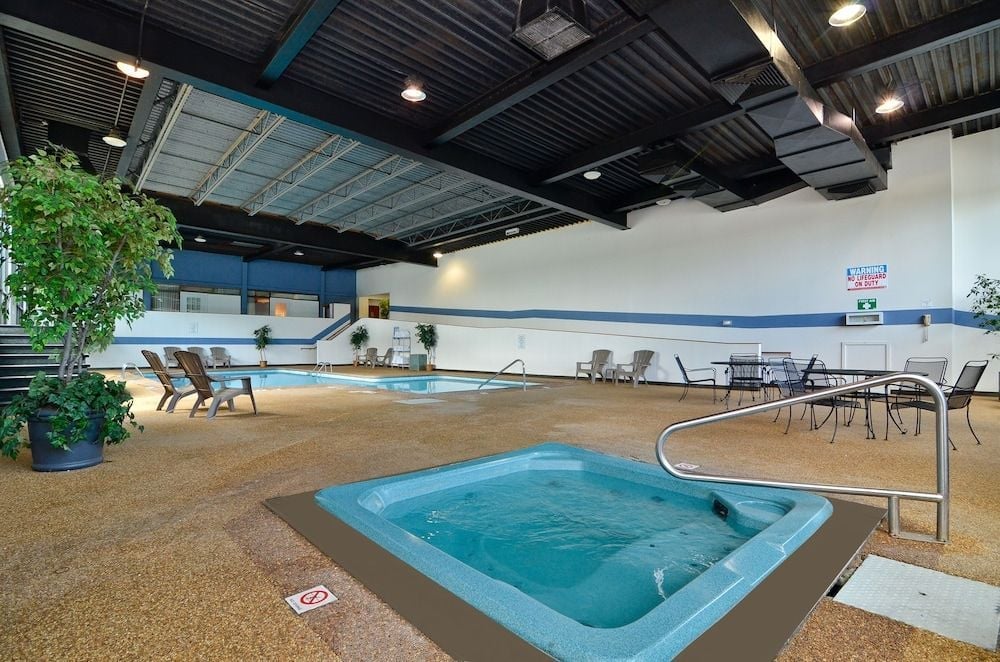 Exposed industrial ceilings frame an inviting aquatic retreat where poolside loungers and bubbling spa create an unexpectedly serene escape beneath dramatic overhead lighting.