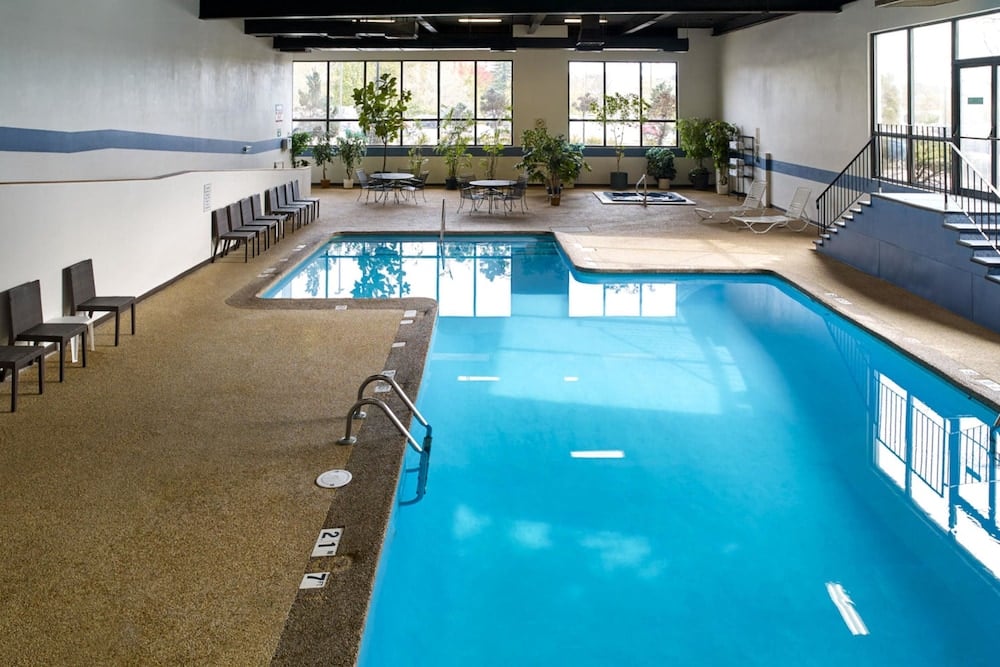 Natural light streams through floor-to-ceiling windows onto the azure indoor pool, where modern seating and potted greenery create an unexpectedly serene urban retreat.